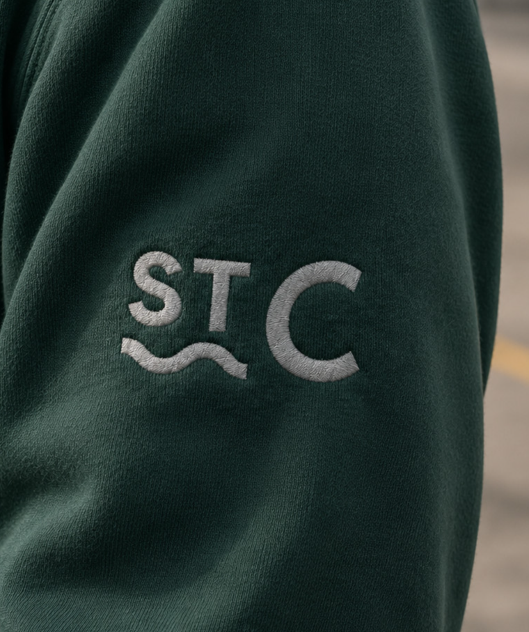 Close-up detail of an embroidered school logo on a dark green uniform sweatshirt, highlighting school identity and branding within an educational setting.