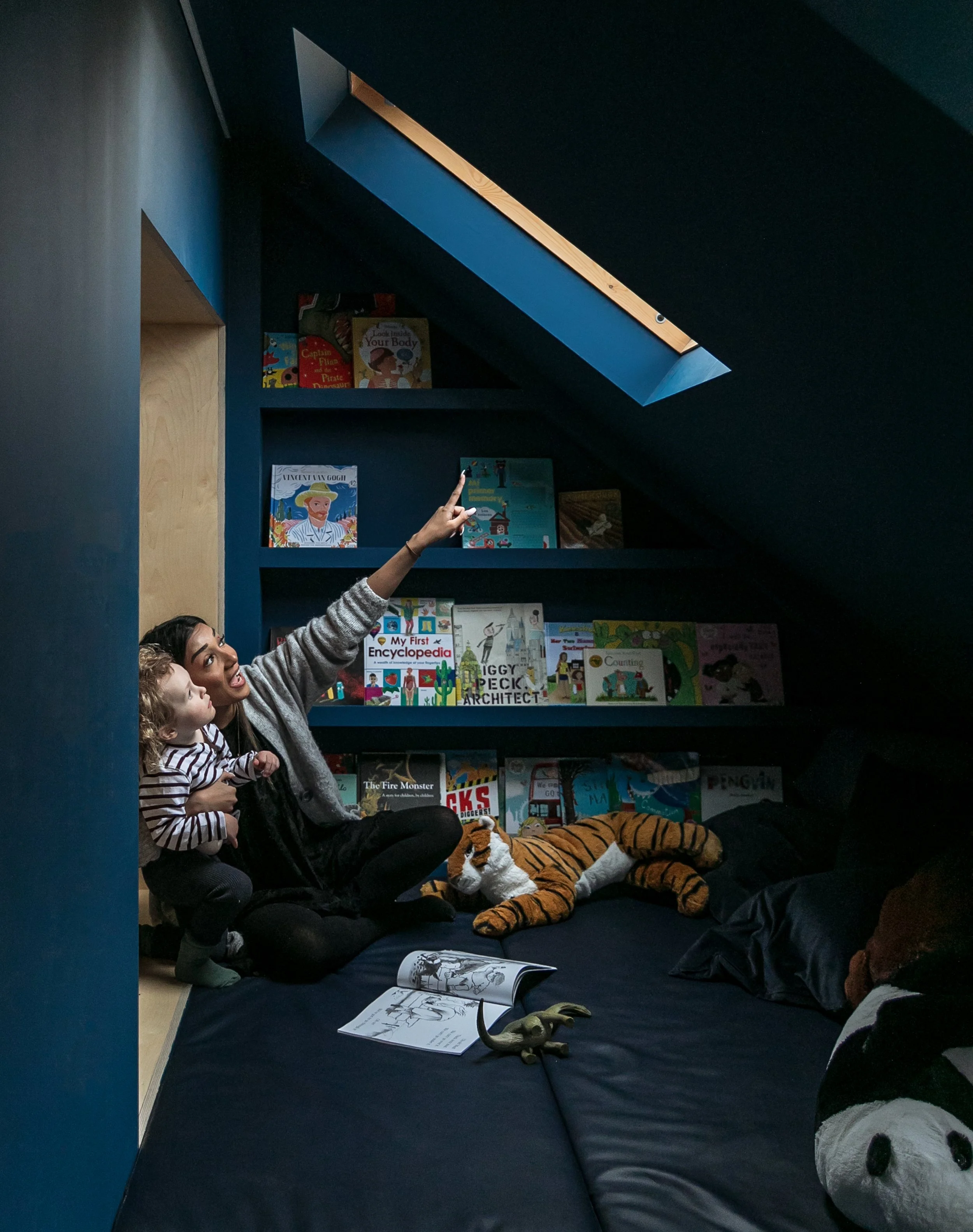 Adult and child in a cosy children’s reading nook with integrated bookshelves, soft seating, and rooflight designed to support quiet learning, storytelling, and wellbeing in an early years environment.