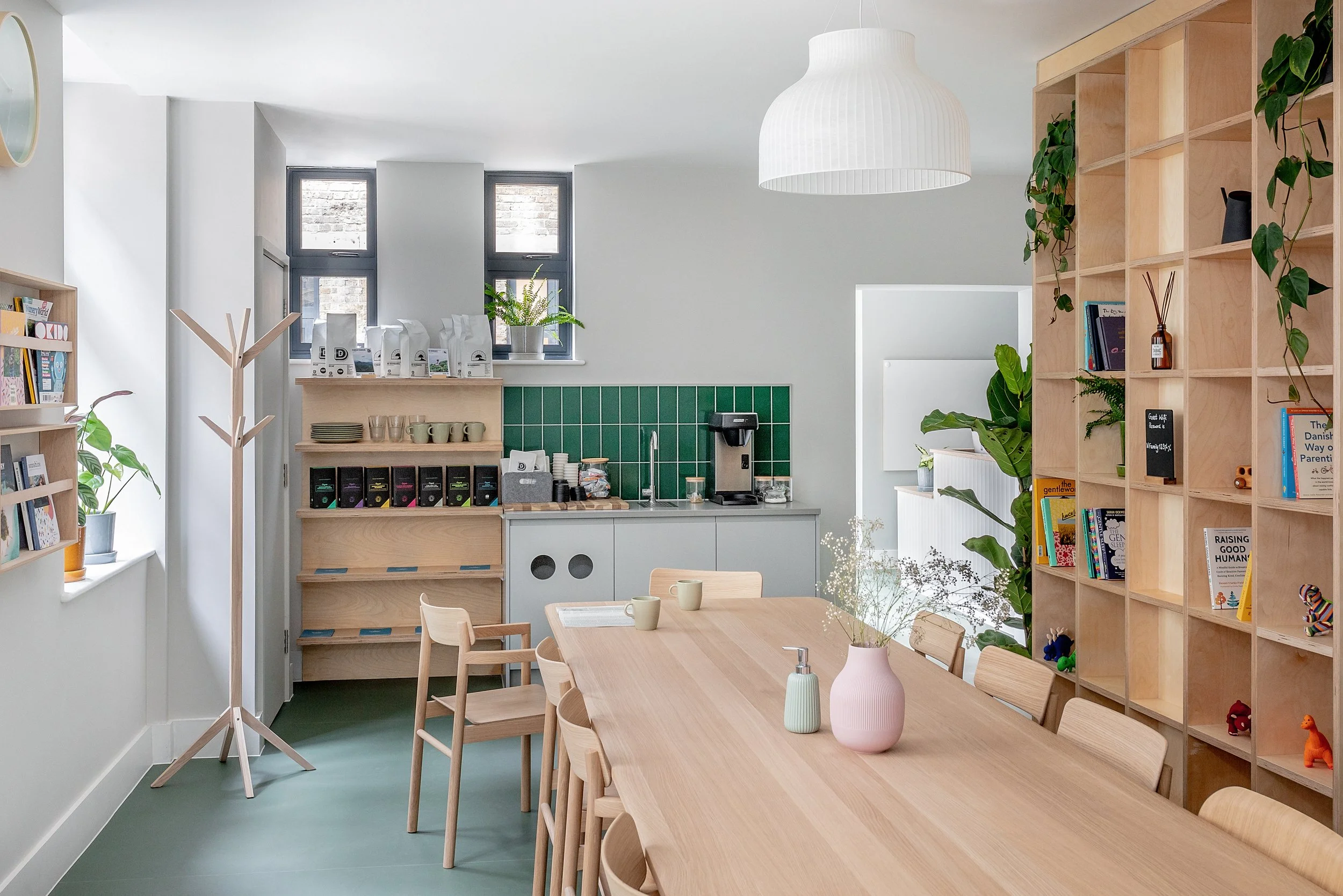 Calm nursery learning interior with timber furniture, open shelving, green tiled kitchenette, and flexible seating designed to support wellbeing, reading, and informal education activities.