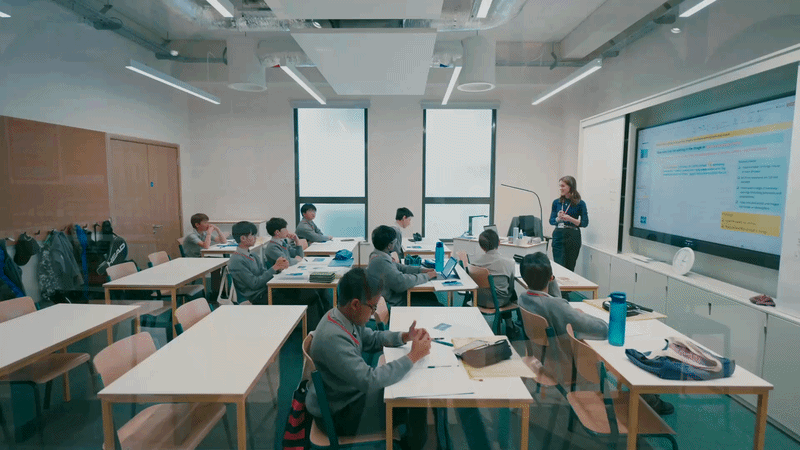 Classroom with students at desks and a teacher at the front near a large screen