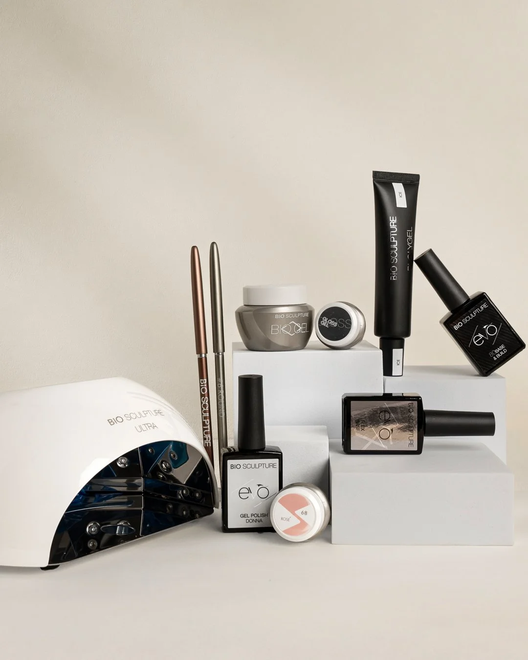 Collection of Bio Sculpture gel nail products and tools including gel polishes, brushes, a nail lamp, and manicure accessories on white platforms.