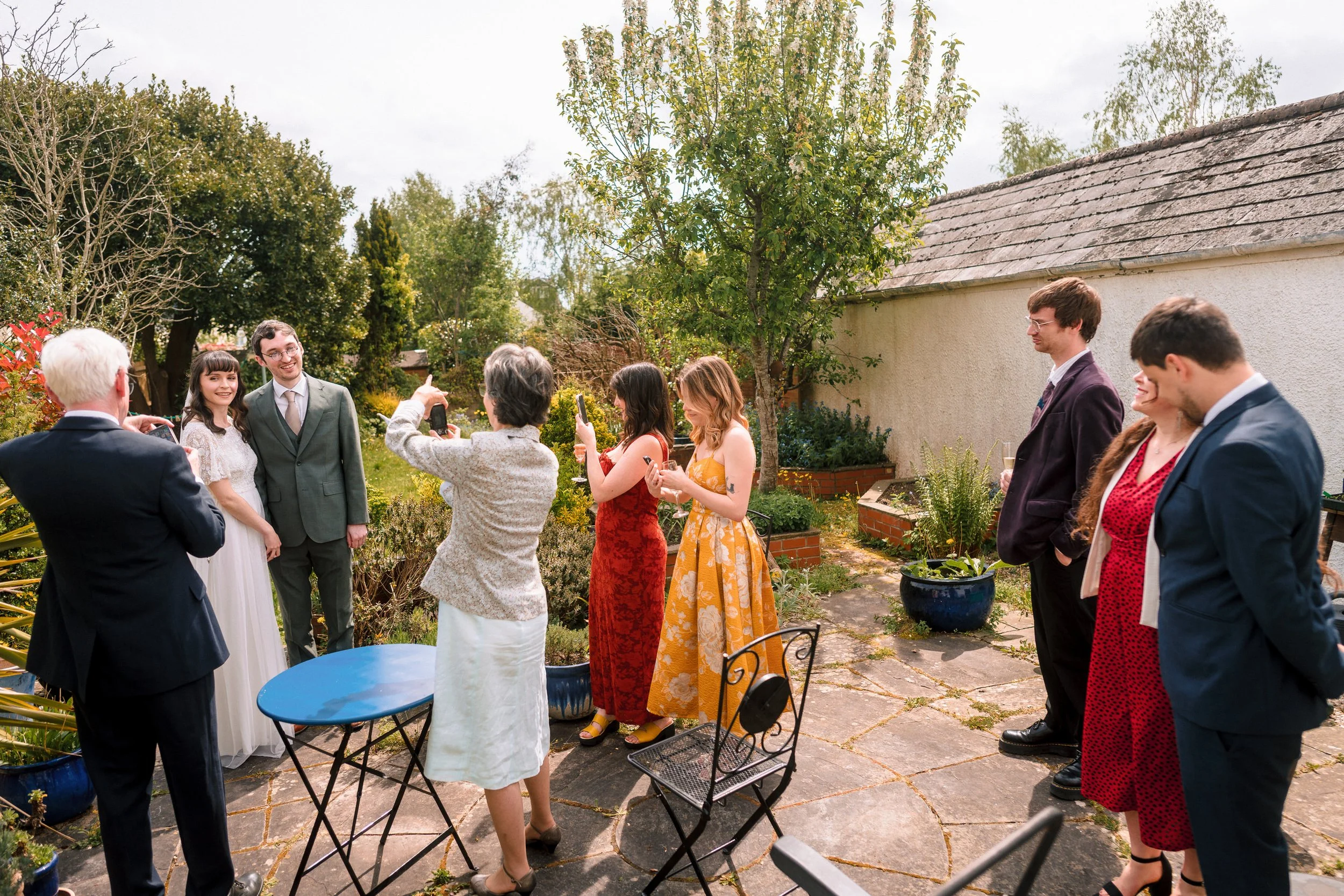Wedding guests mingling in a garden courtyard beside a rustic house