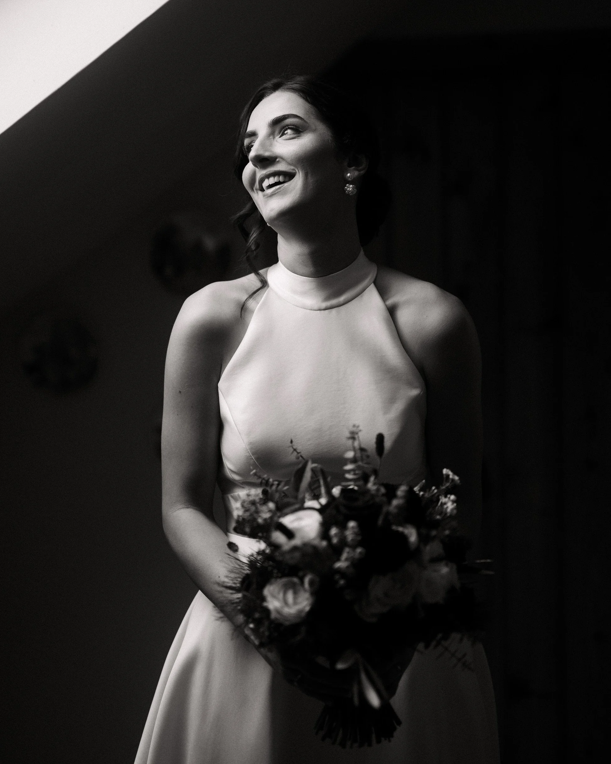 Black-and-white portrait of a smiling woman in a high-neck wedding dress holding a bouquet of flowers