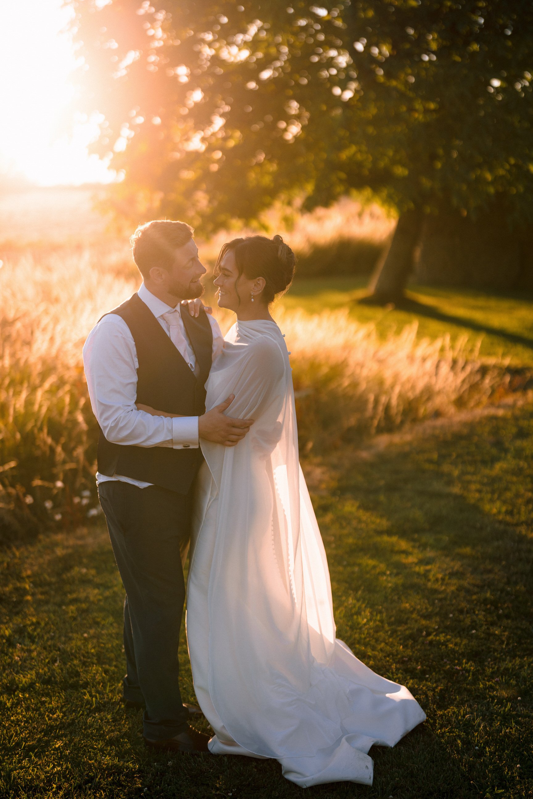 Newlywed couple embracing outdoors in a sunlit field at golden hour