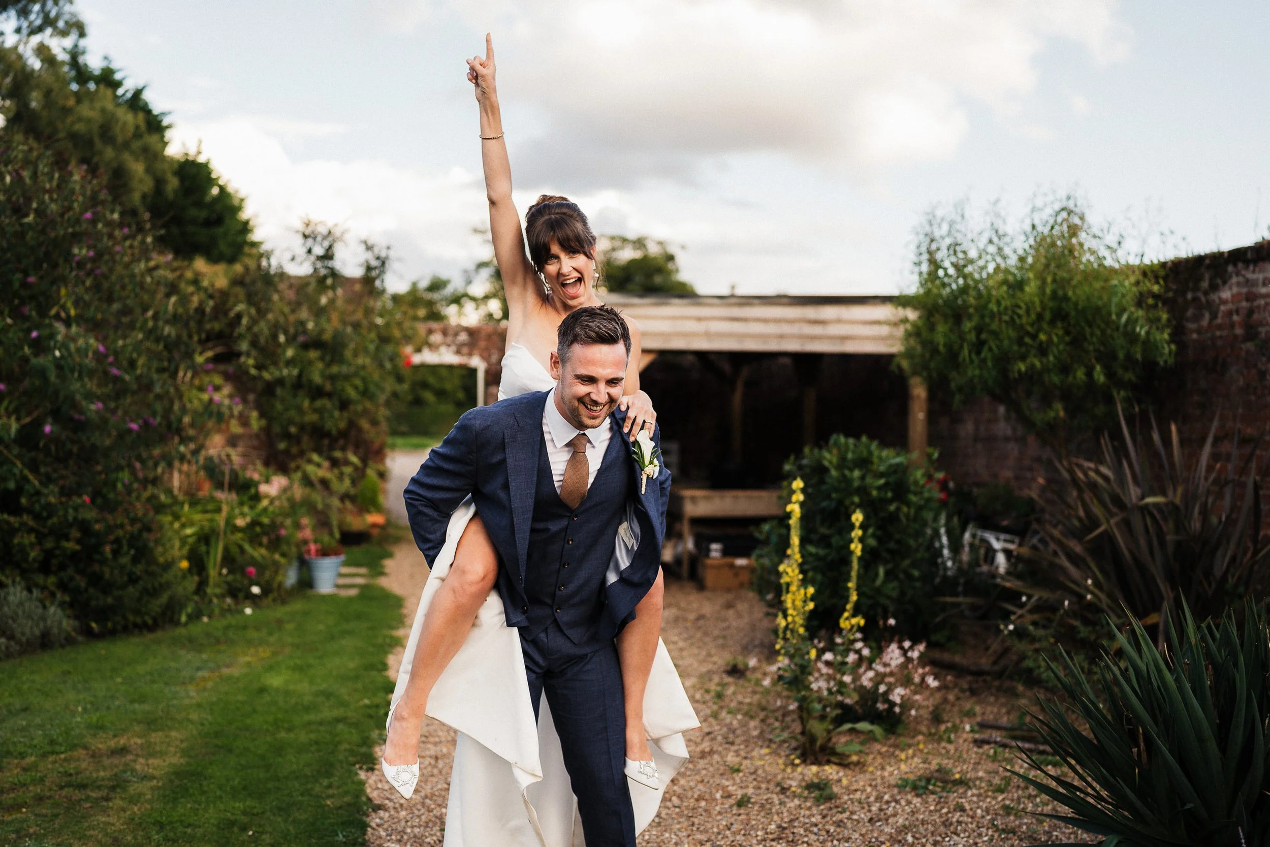 Groom carrying laughing bride in a wedding dress through a garden