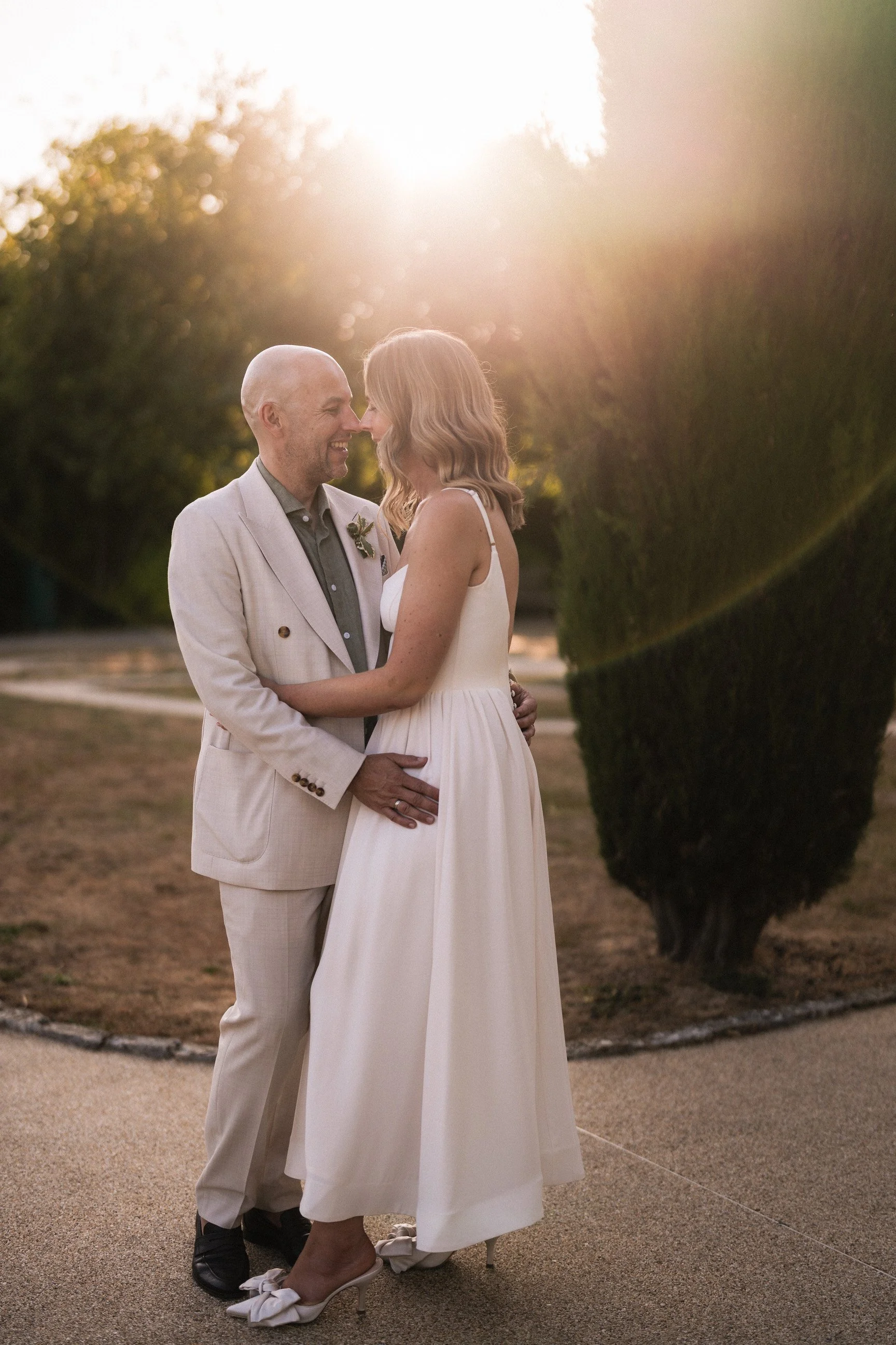 Couple embracing and smiling in wedding attire outdoors at sunset