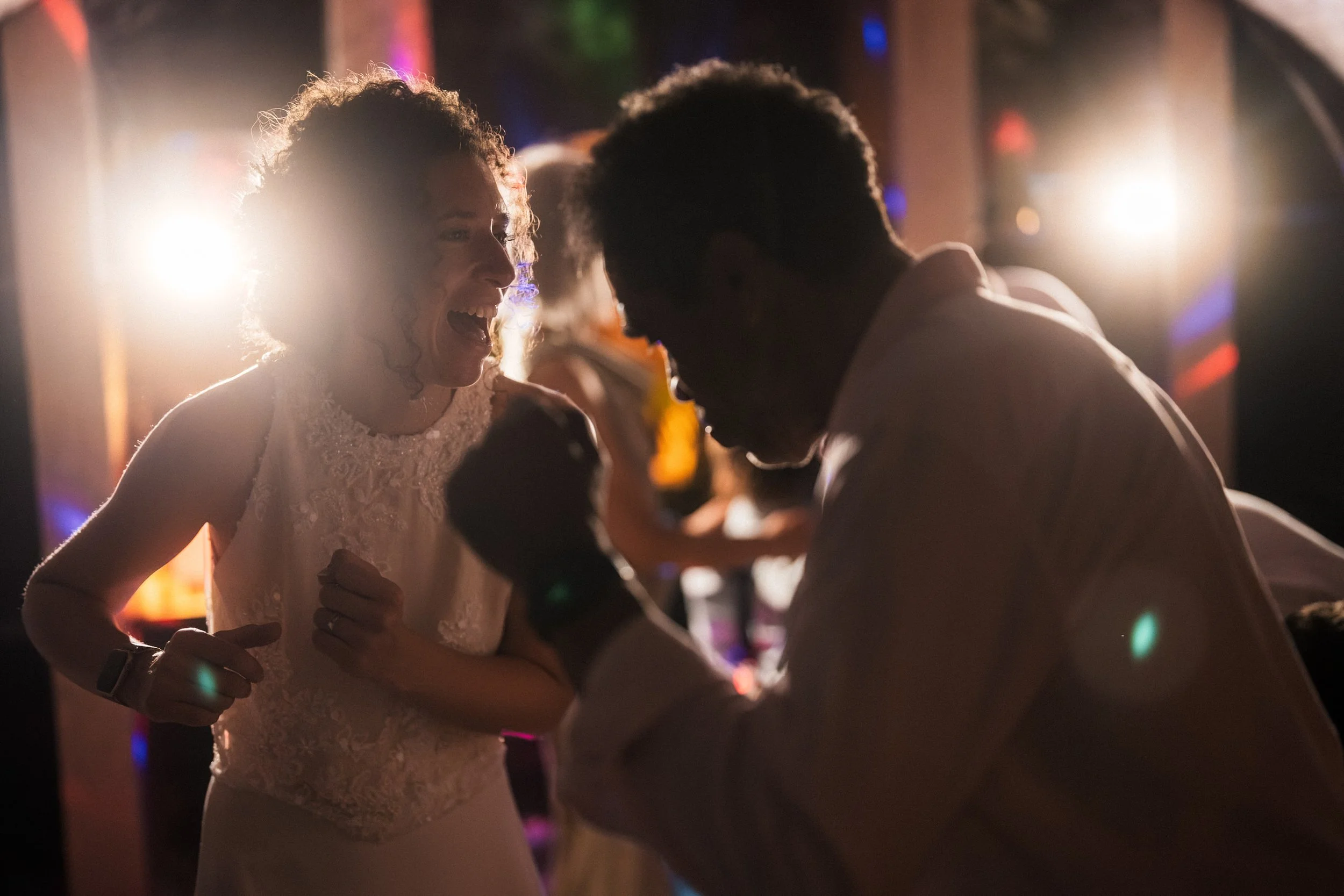 Bride and groom embracing and smiling at a colorful wedding reception.