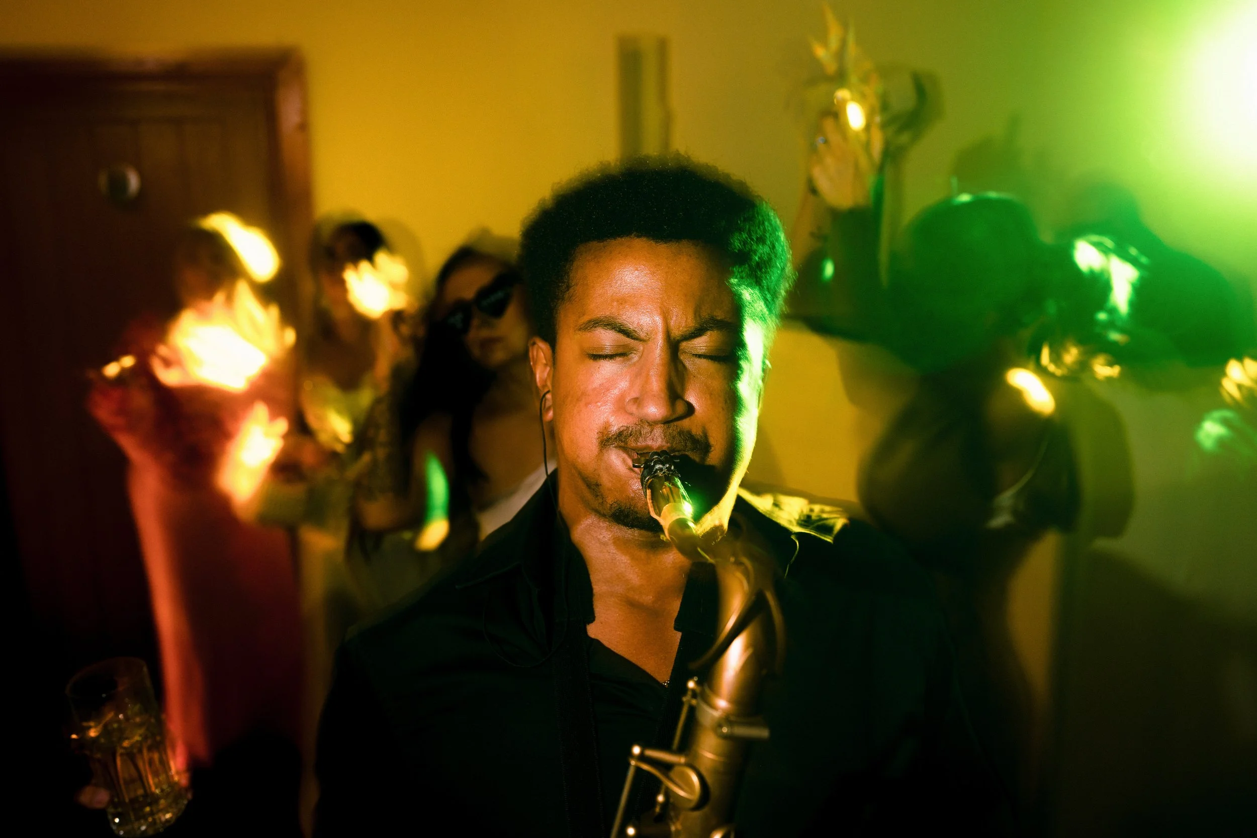 Jazz saxophonist performing with a band under colorful green and yellow stage lights