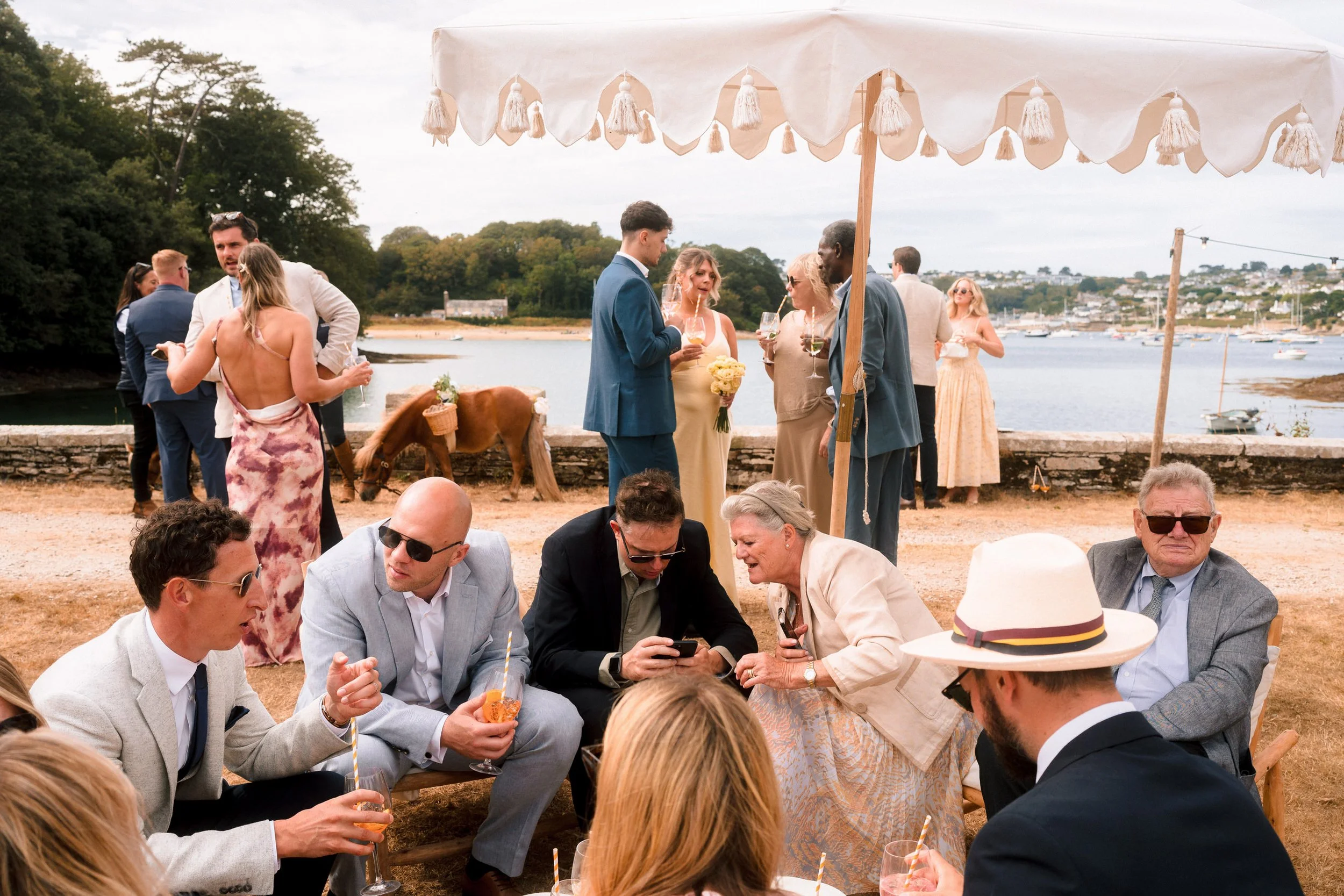 Guests enjoying an outdoor wedding reception under a tasseled canopy overlooking a harbor