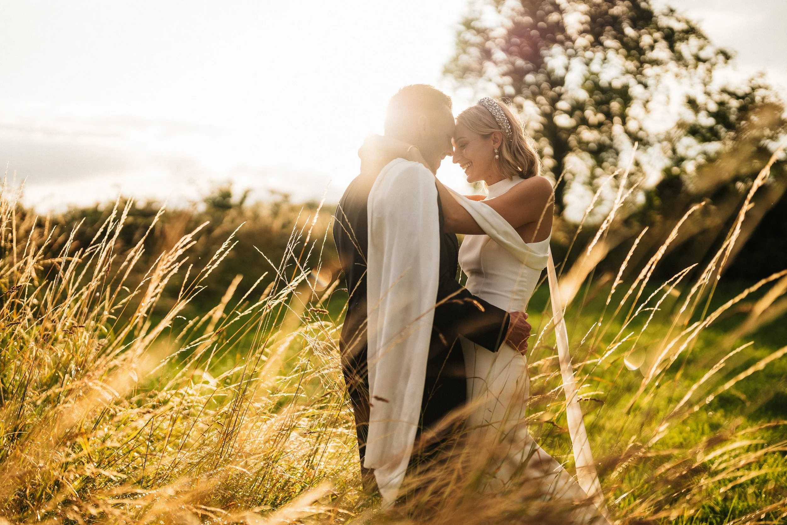 Bride and groom embracing in a sunlit field of tall grass