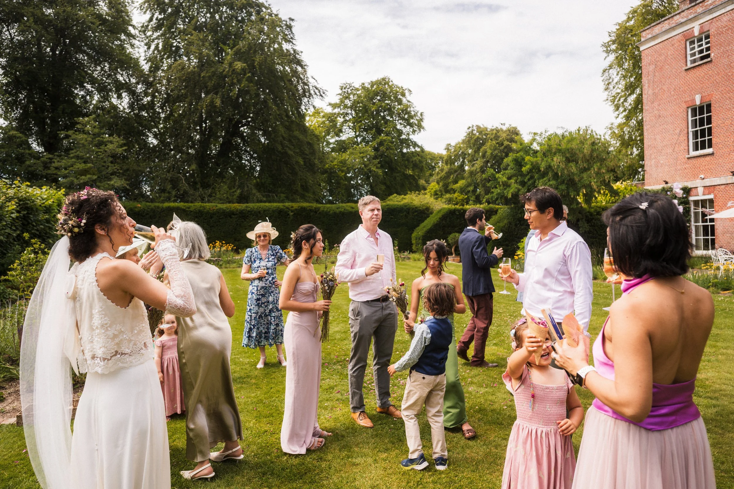 Wedding guests enjoying drinks in a garden beside a red brick building