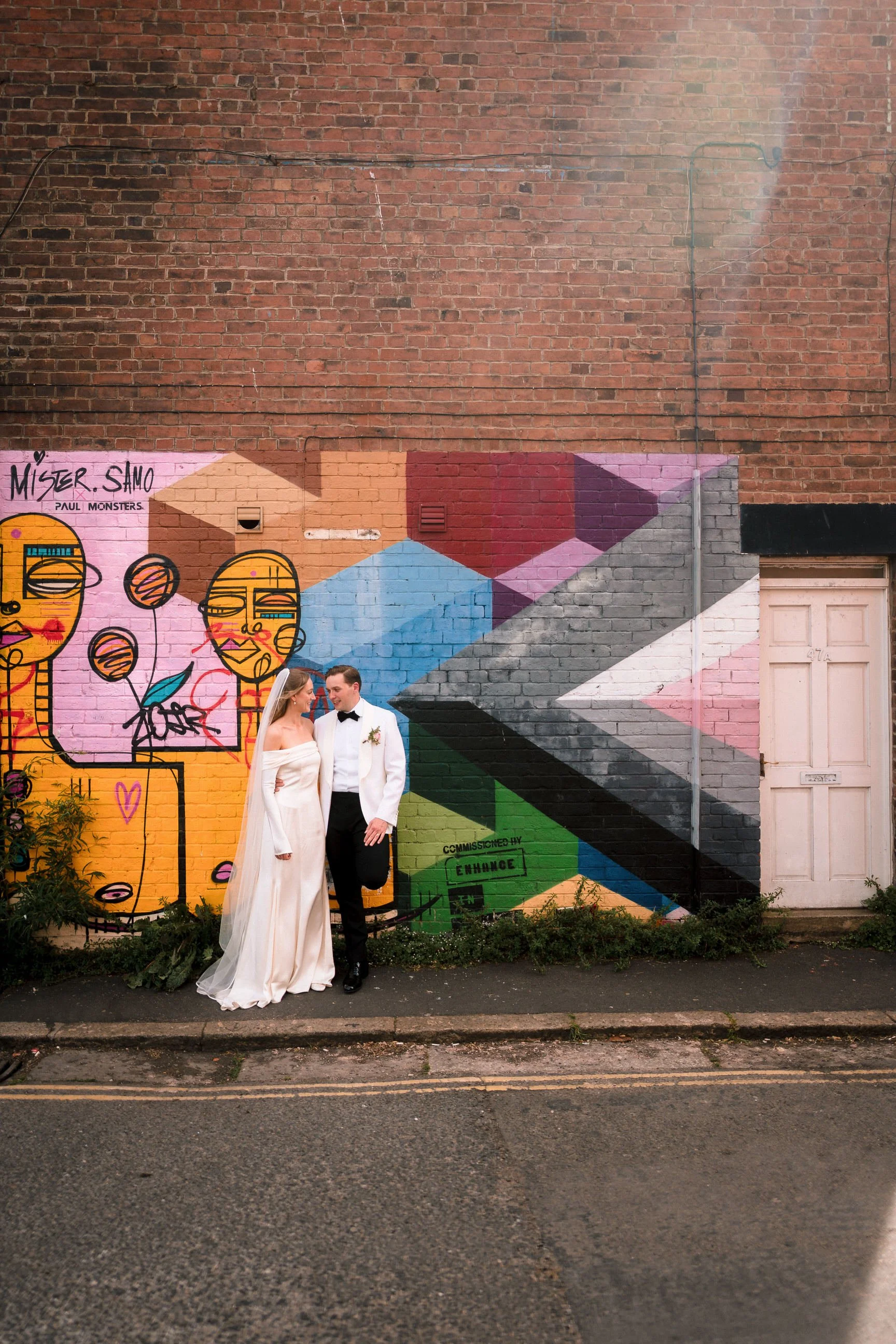 Newlywed bride and groom posing beside a colorful graffiti mural on a brick wall