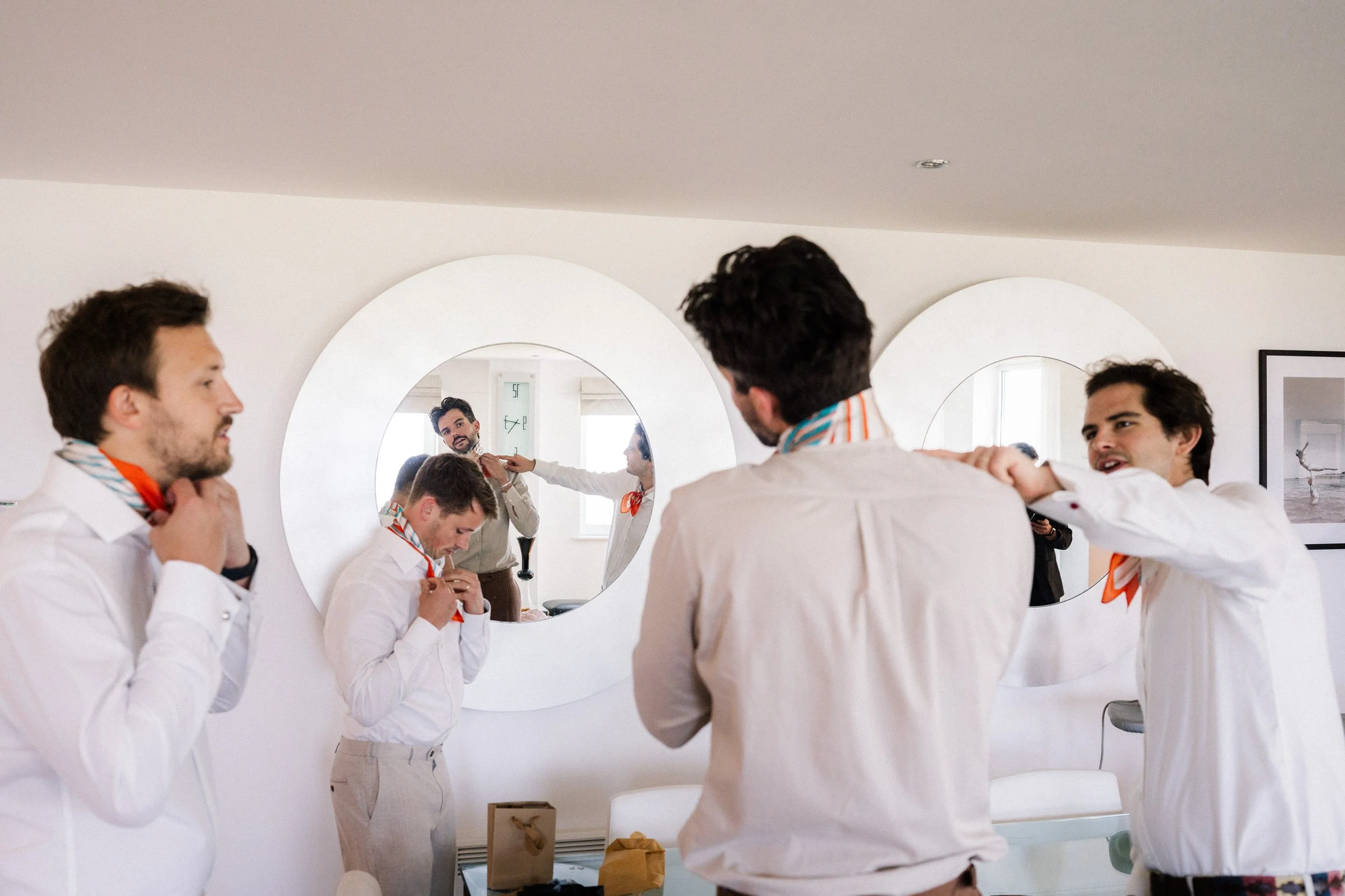 Group of men adjusting colorful neckerchiefs in front of round mirrors