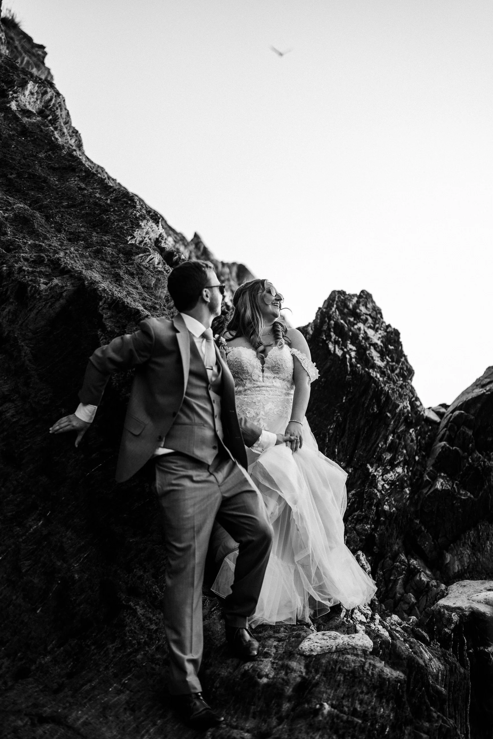 Black-and-white portrait of a bride and groom posing on rugged mountain rocks.
