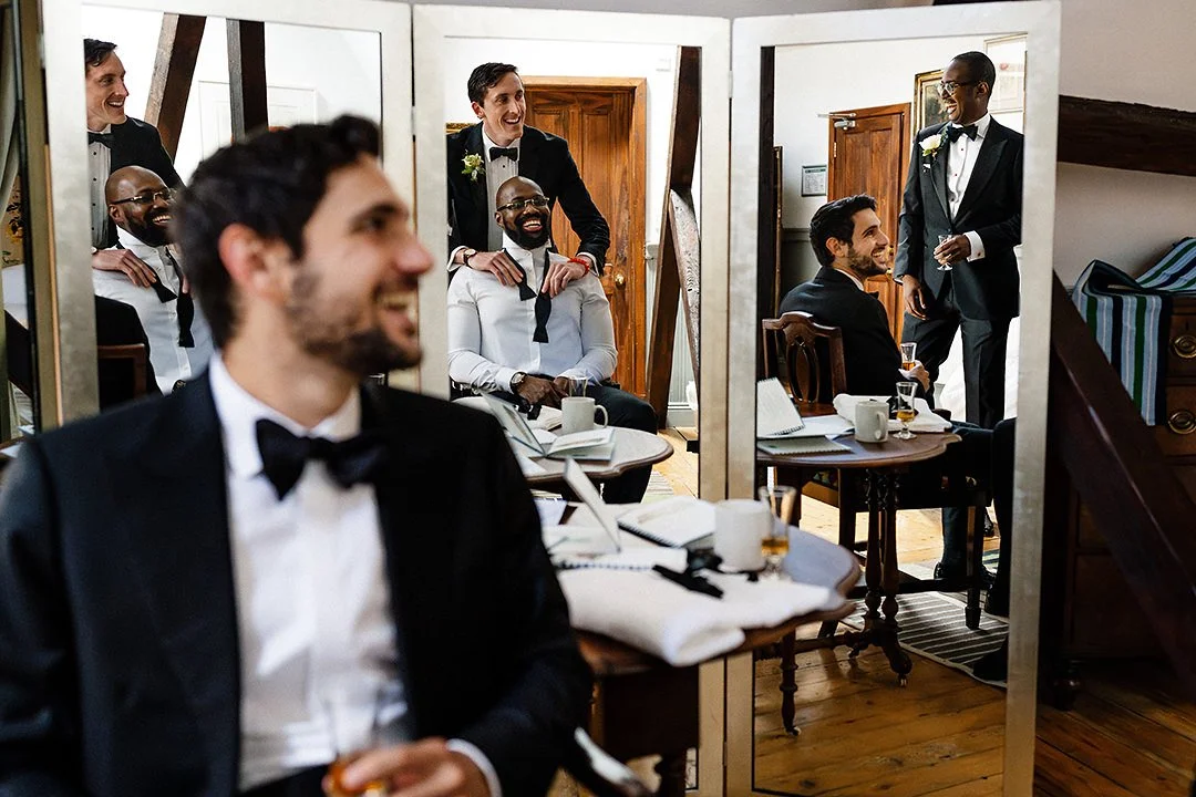 Groomsmen in tuxedos laughing and relaxing in a dressing room before a wedding.