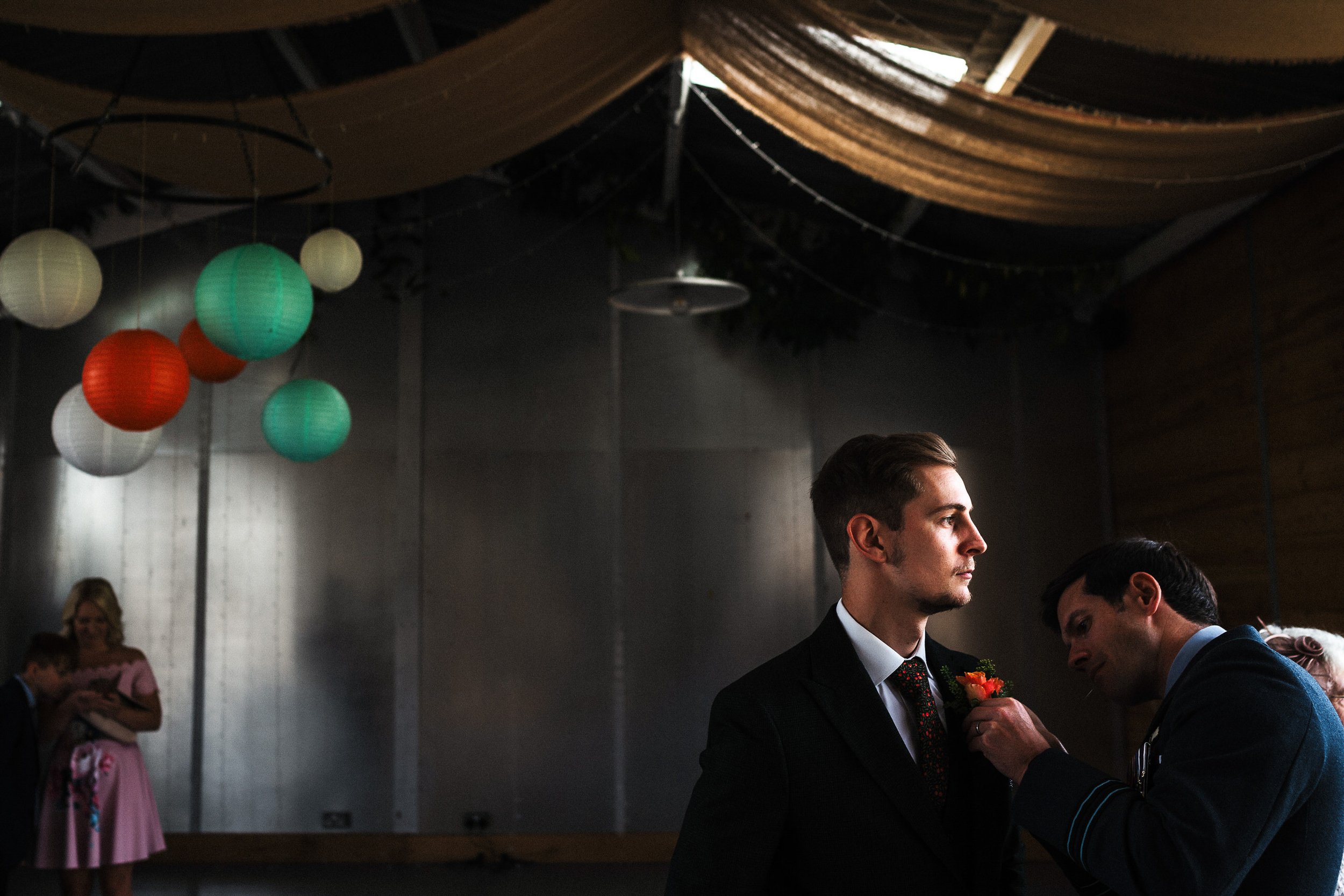 Wedding reception with a groom in a black suit, colorful hanging lanterns, and guests in the background