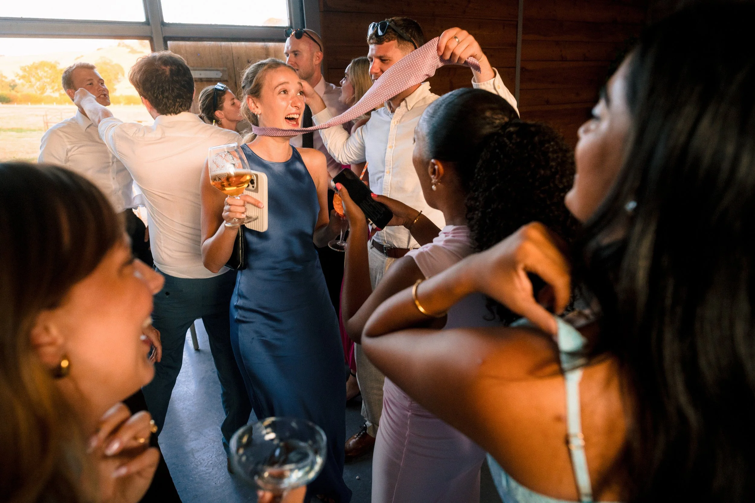 Group of friends celebrating indoors with drinks and a playful pink tie game