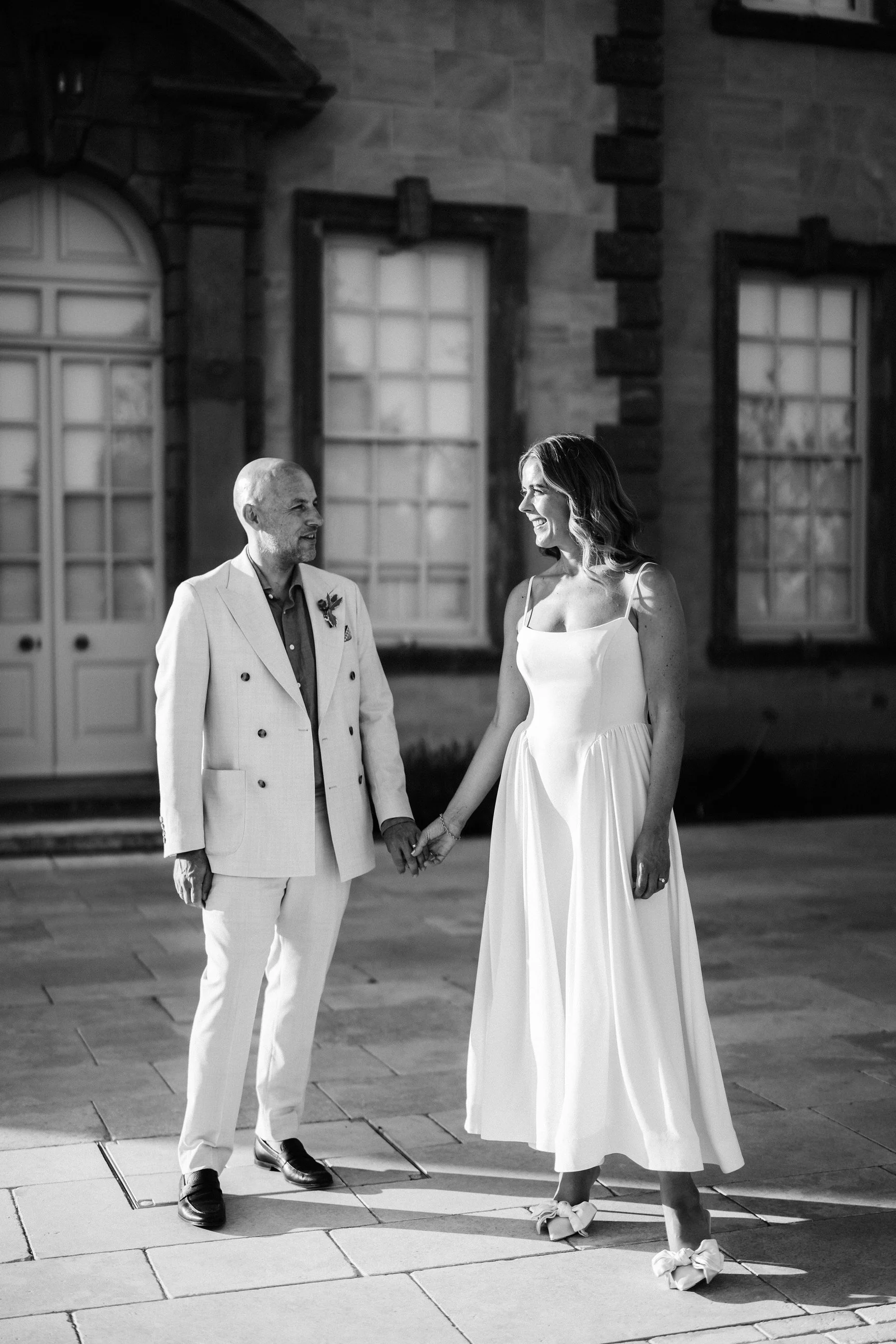 Black-and-white wedding portrait of a smiling couple holding hands outside a historic building