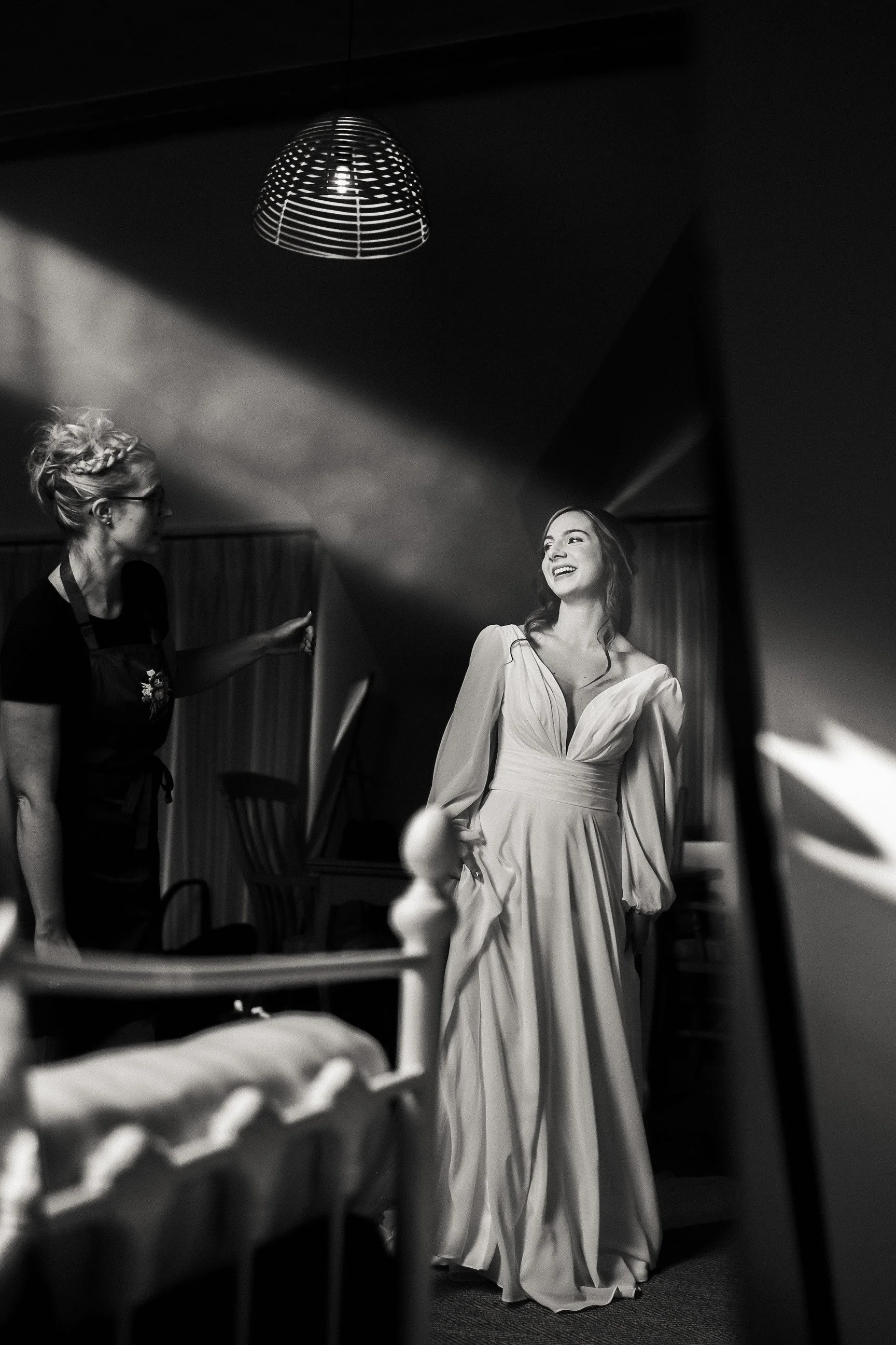 Black-and-white backstage photo of a smiling woman in a flowing gown beside a crew member under a stage light.