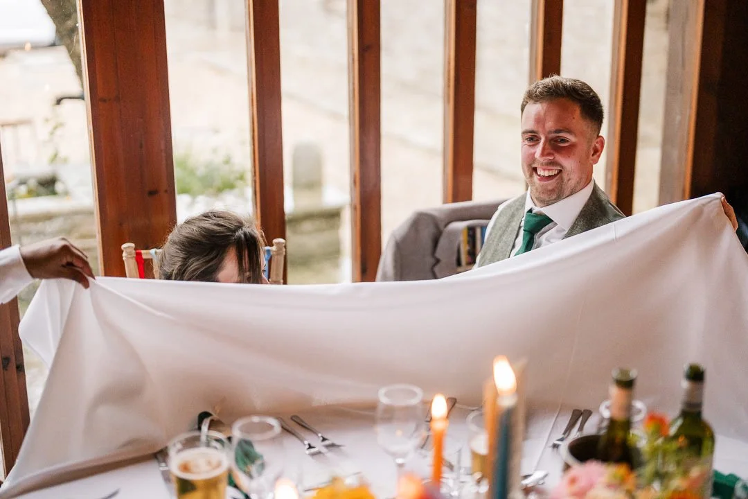 Smiling groom holding a white tablecloth during a wedding reception dinner