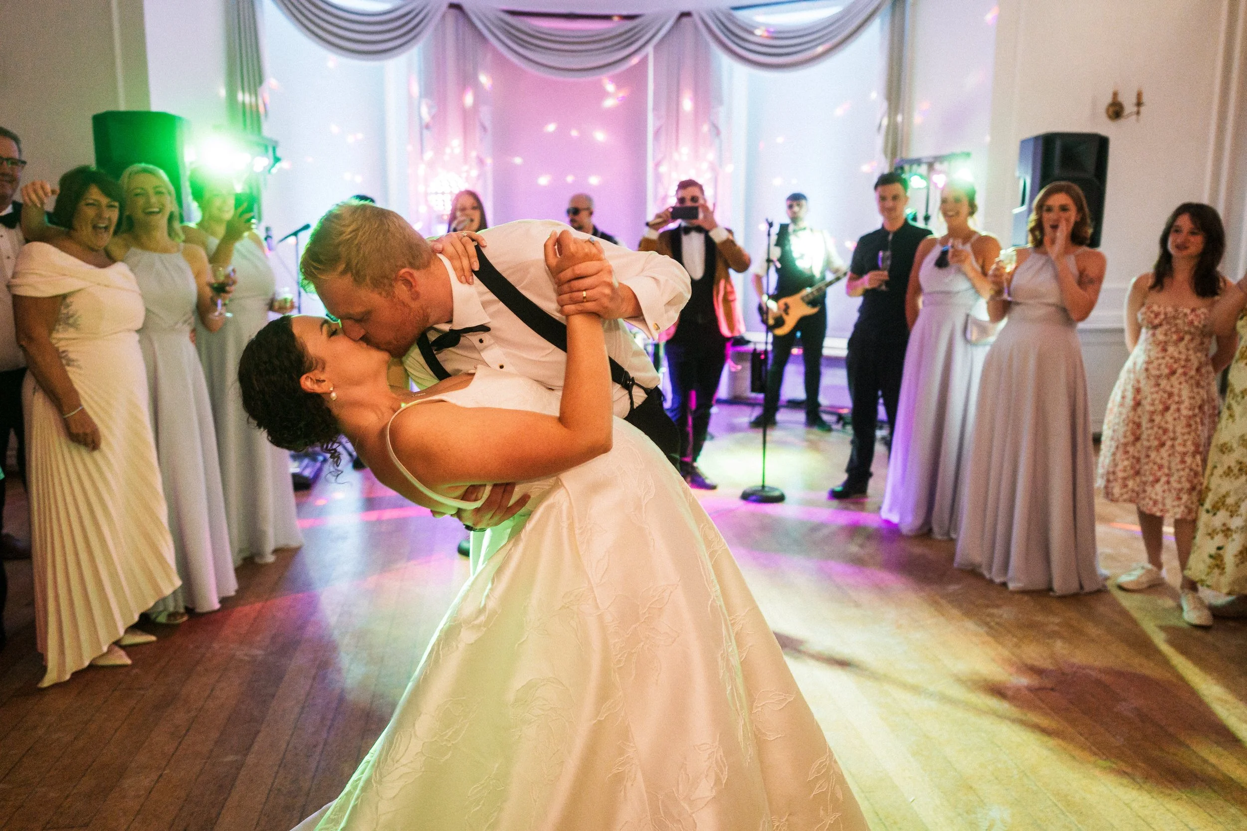 Bride and groom kissing during a wedding reception as guests watch and a live band performs.