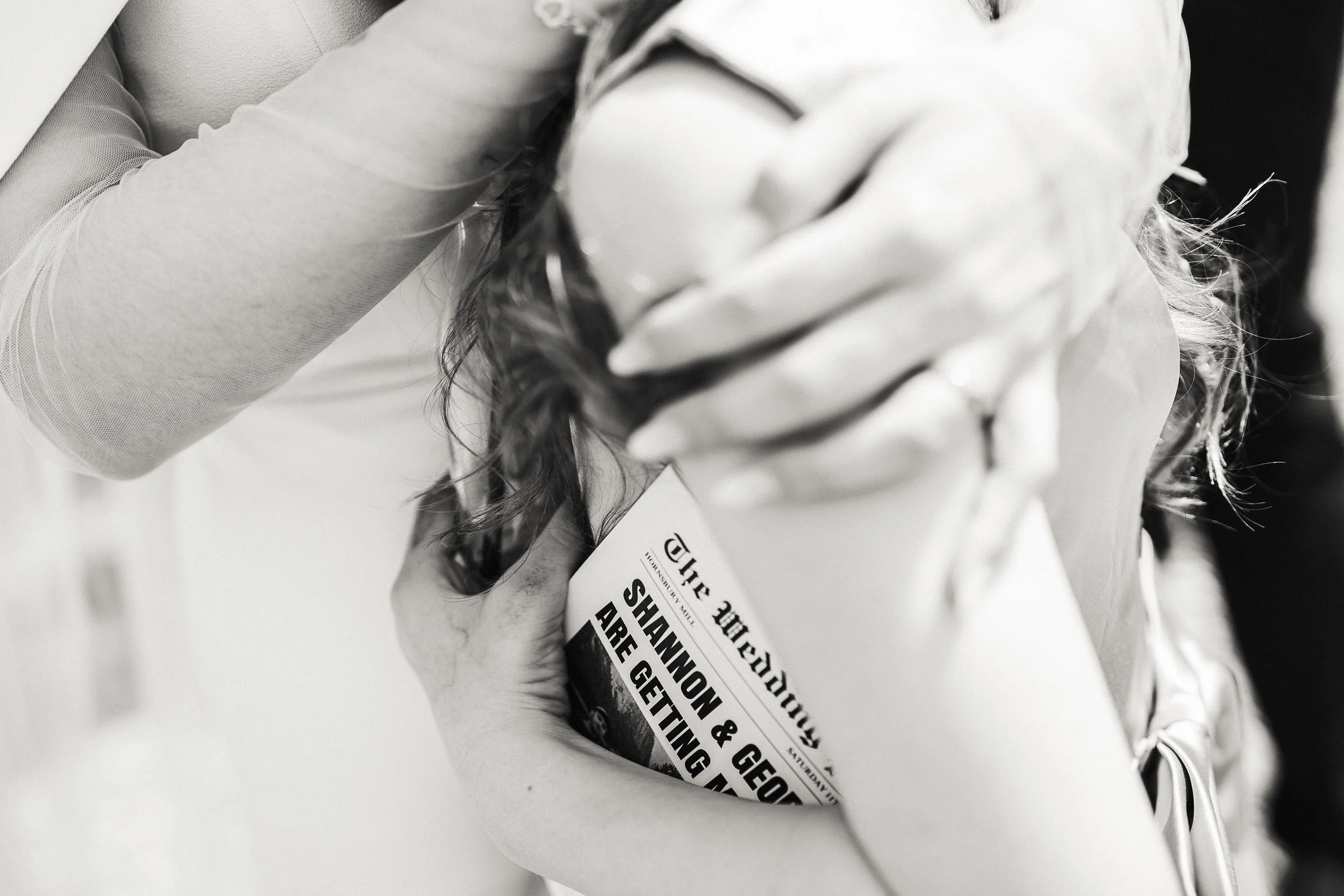 Black-and-white close-up of a smiling bride reading a wedding planning magazine titled “Shannon & Geo Are Getting Married.”
