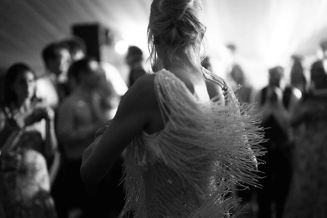 Black-and-white photo of a woman in a feathered dress dancing at a crowded party.