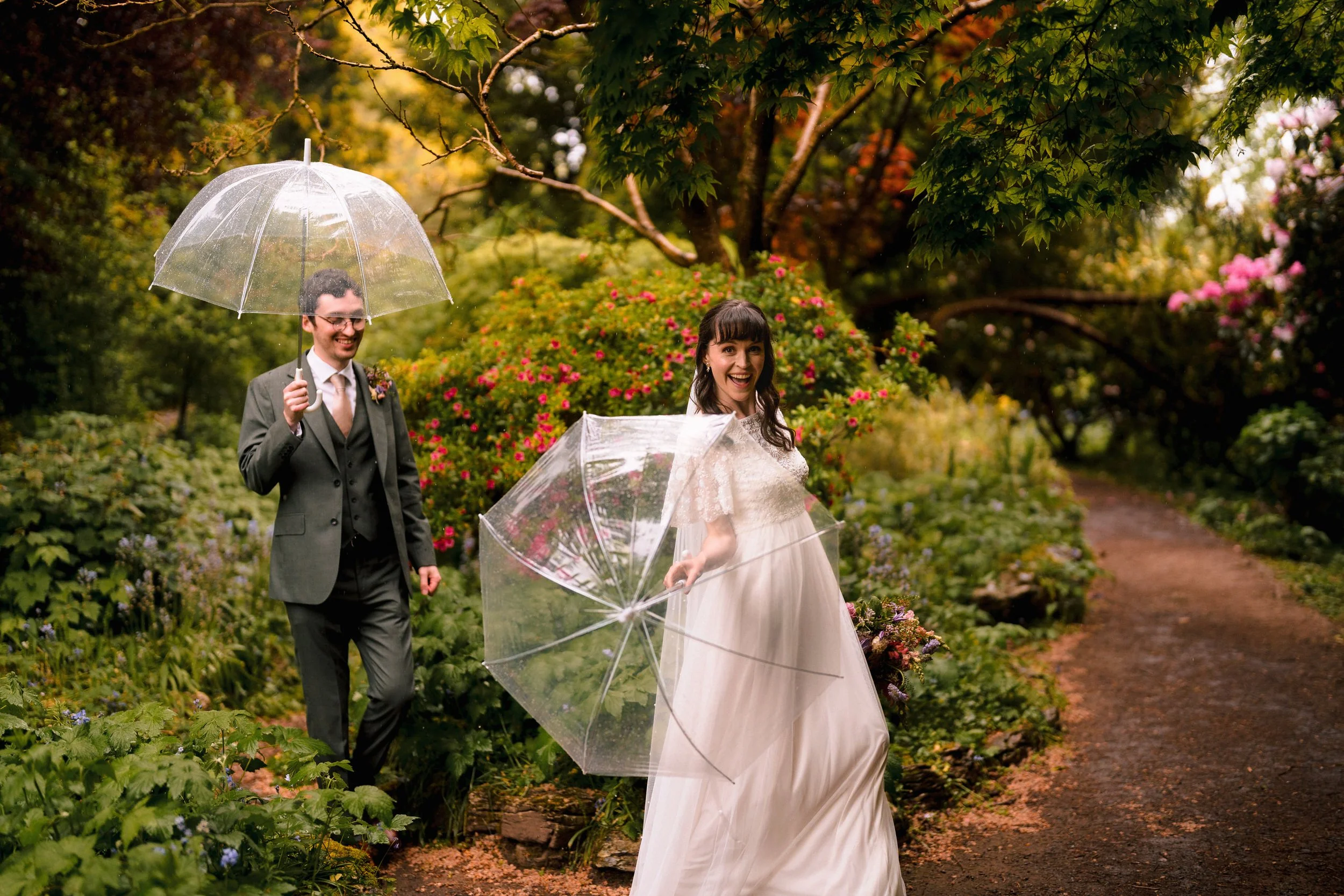 Bride and groom carrying clear umbrellas through a flower-filled garden on a rainy wedding day