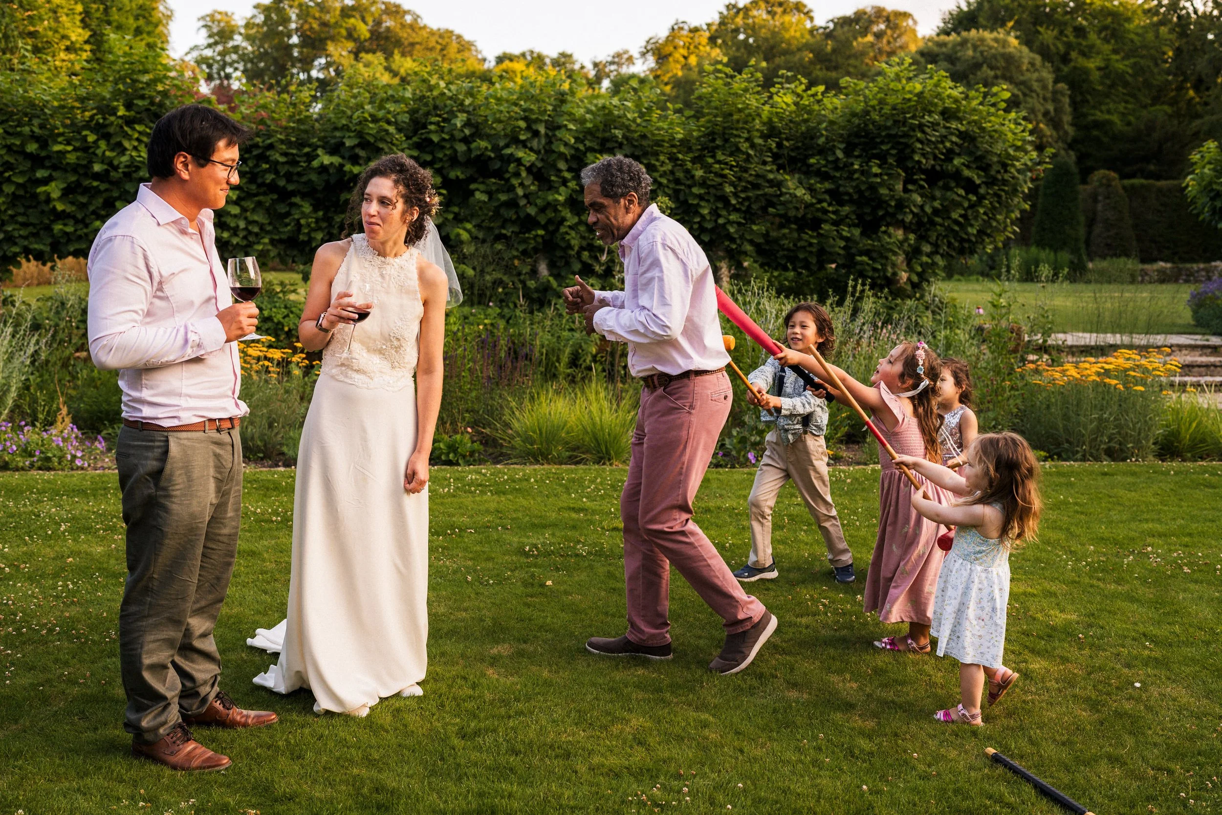 Bride and wedding guests enjoying wine and playing with children in a garden
