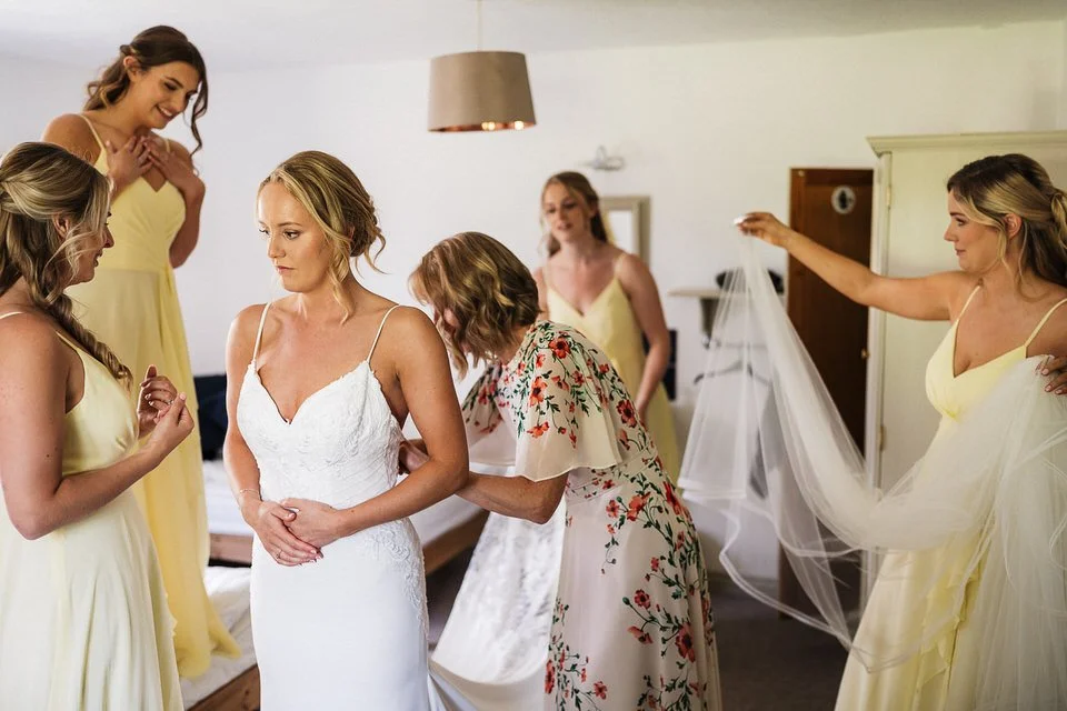 Bride in a white wedding dress surrounded by bridesmaids preparing for the ceremony.