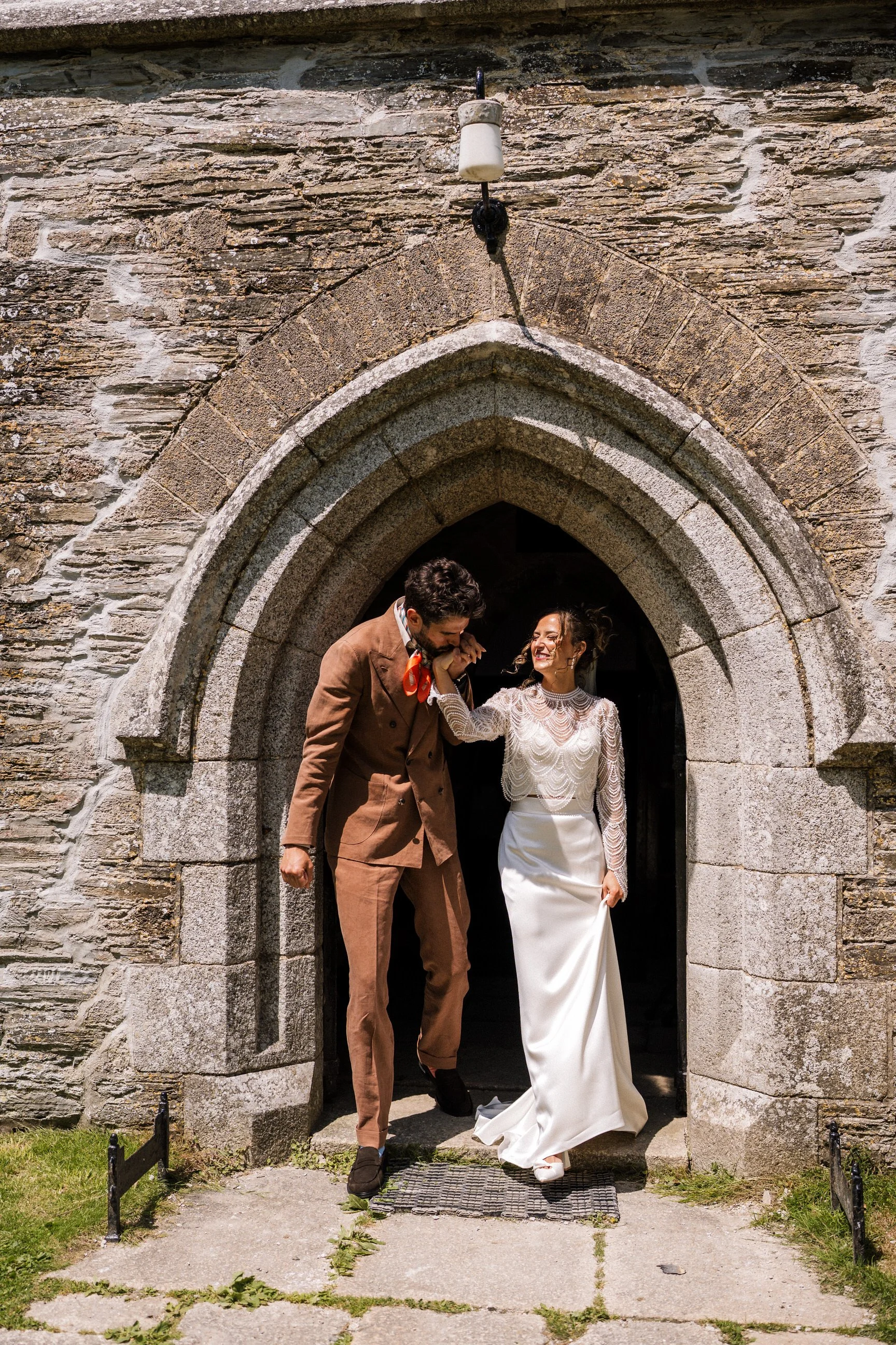 Bride and groom leaving a historic stone church through an arched doorway.