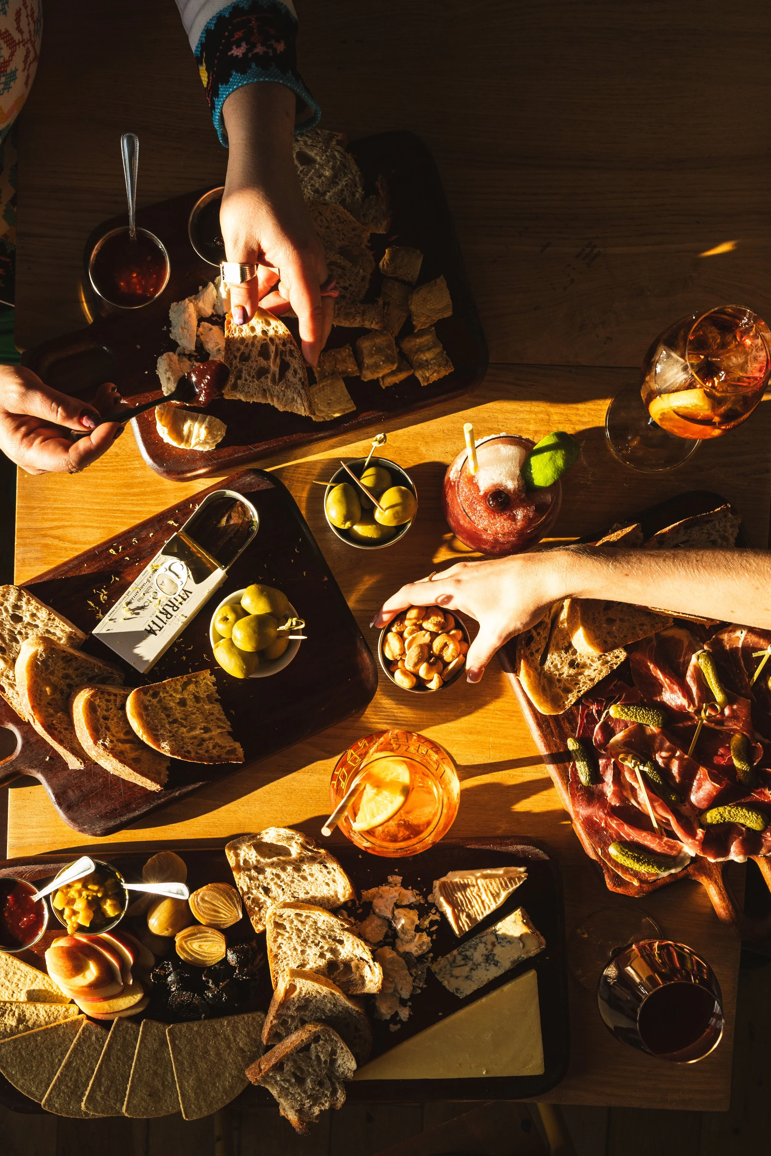 A table with assorted bread, cheese, olives, nuts, and various drinks including wine and cocktails, part of the deli offering and picky bits available at Little Swift bar Margate.