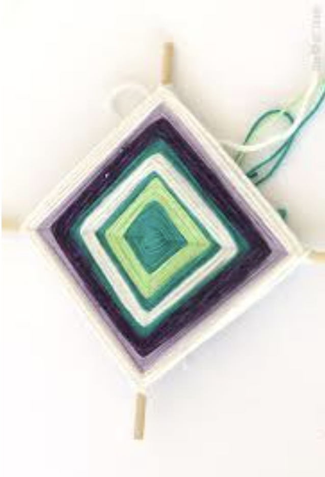 Image of a God's Eye. Green, white, and purple yarn is stretched across two crossed sticks to form a square design.