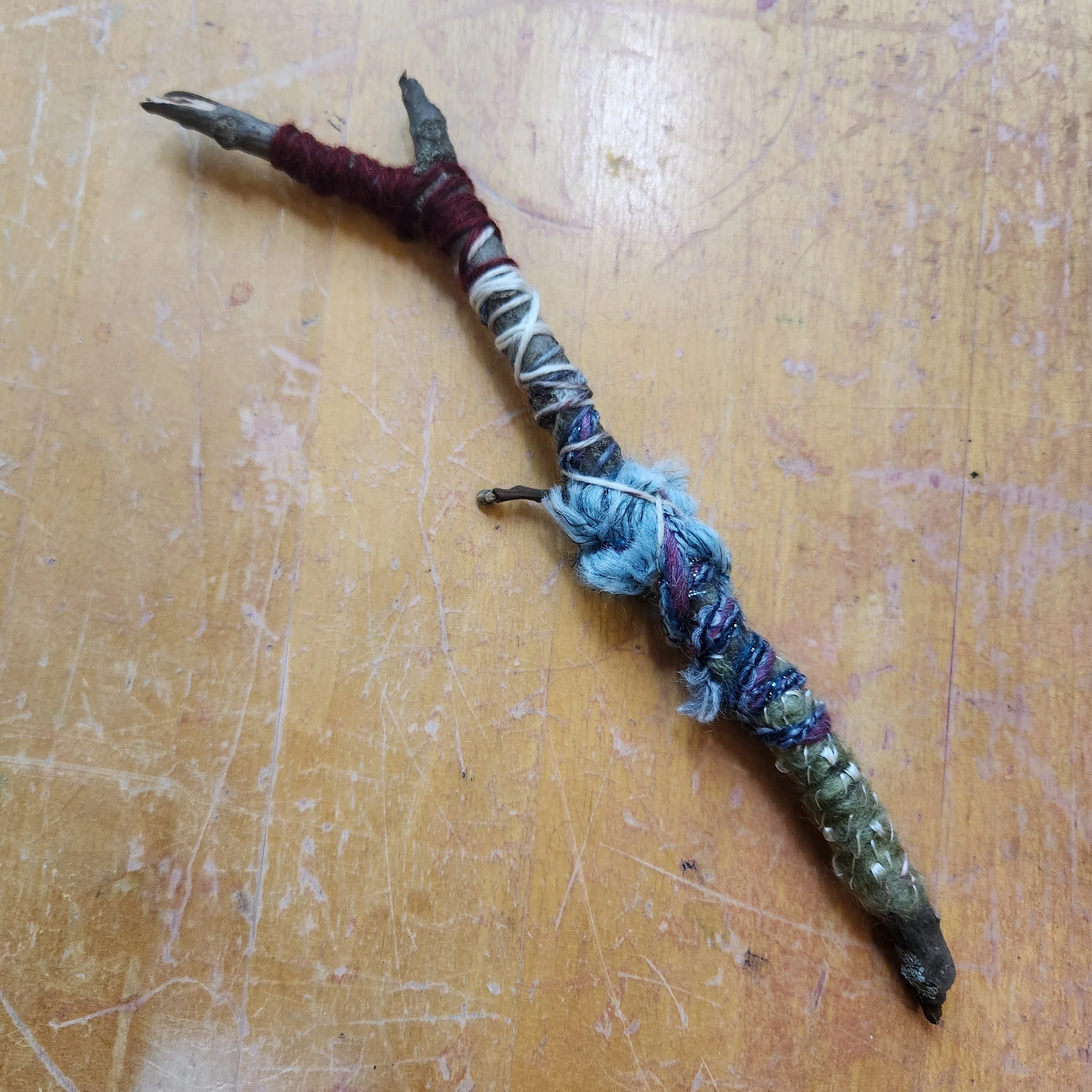 A wooden stick wrapped in blue, purple, white, red, and green yarn.