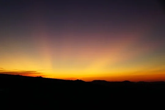 Sunset over a silhouetted landscape with a colorful sky.