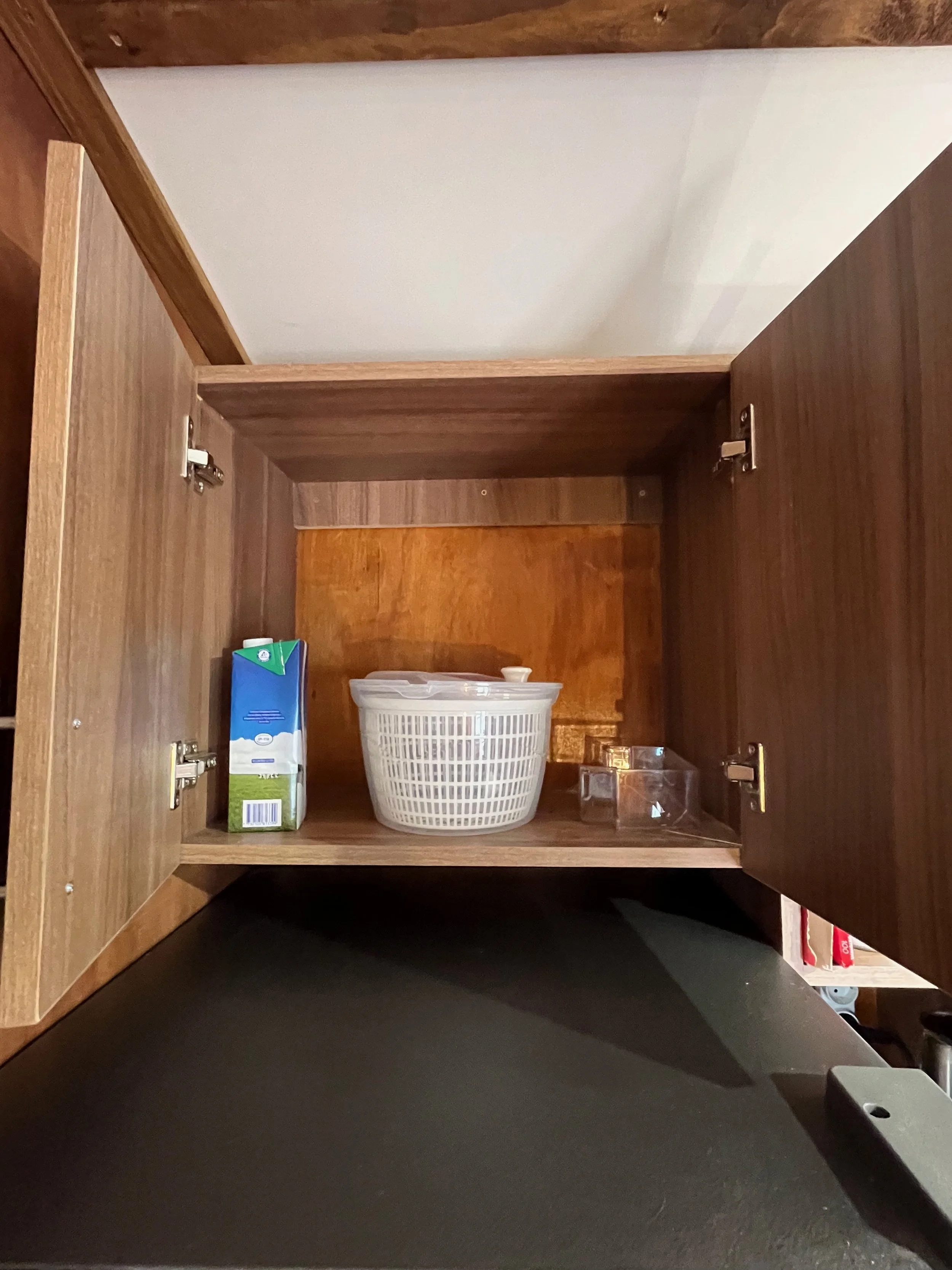 Empty kitchen cabinet with a plastic basket, a carton, and some small containers inside.