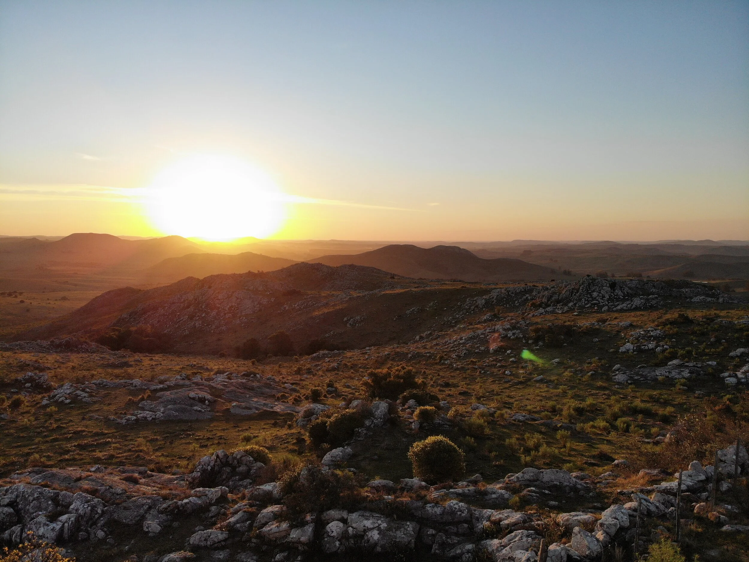 Sunset over rocky hills and grasslands with a clear sky.