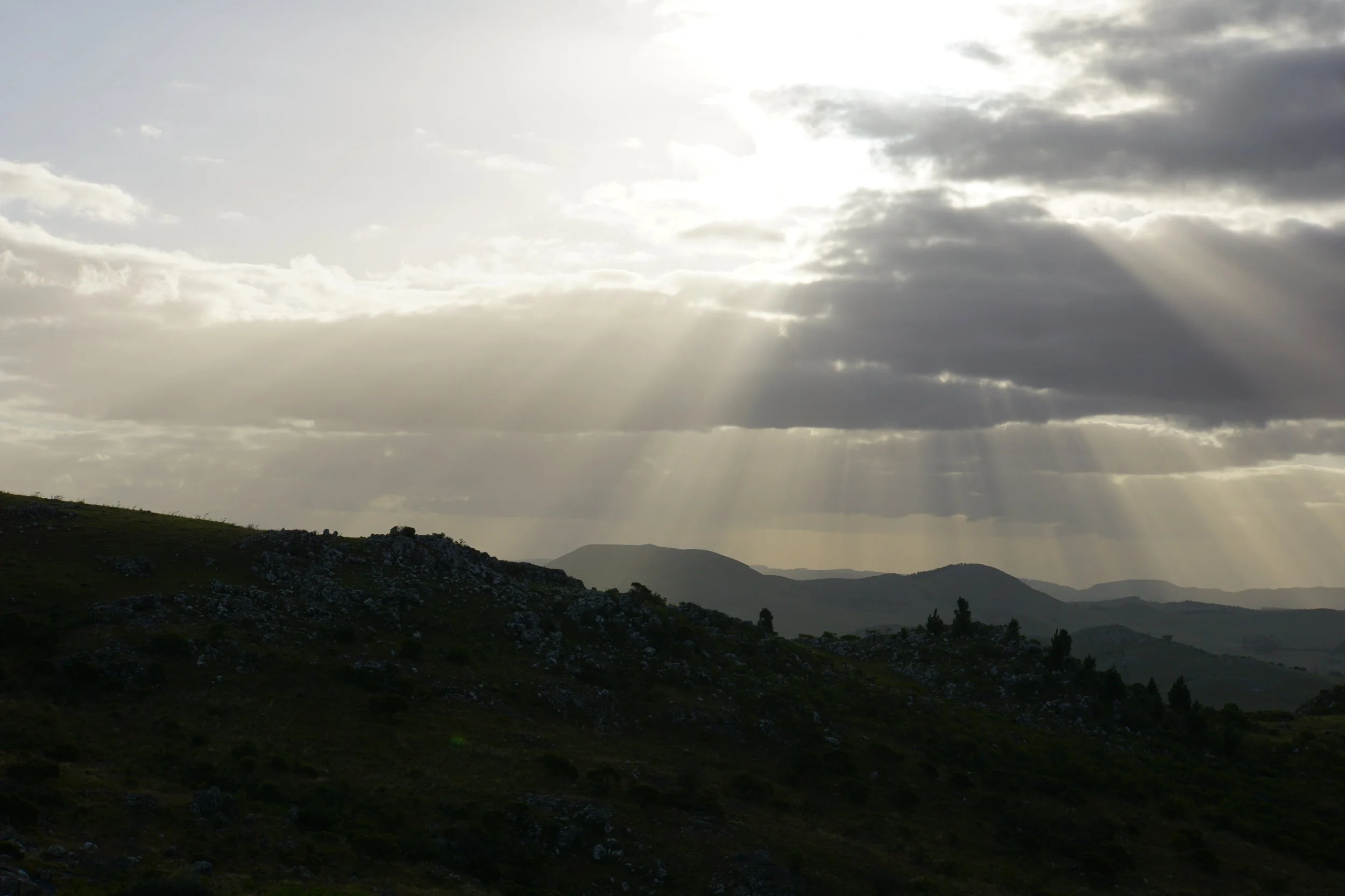 Sun rays breaking through cloudy sky over rolling hills and mountains