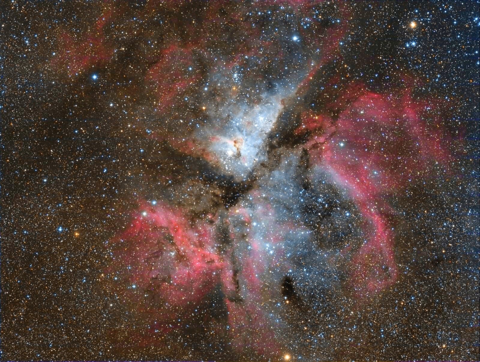 A vivid image of outer space showing a dense nebula with bright, colorful clouds of gas and dust, many stars of varying brightness, and different shades of red, blue, and black.