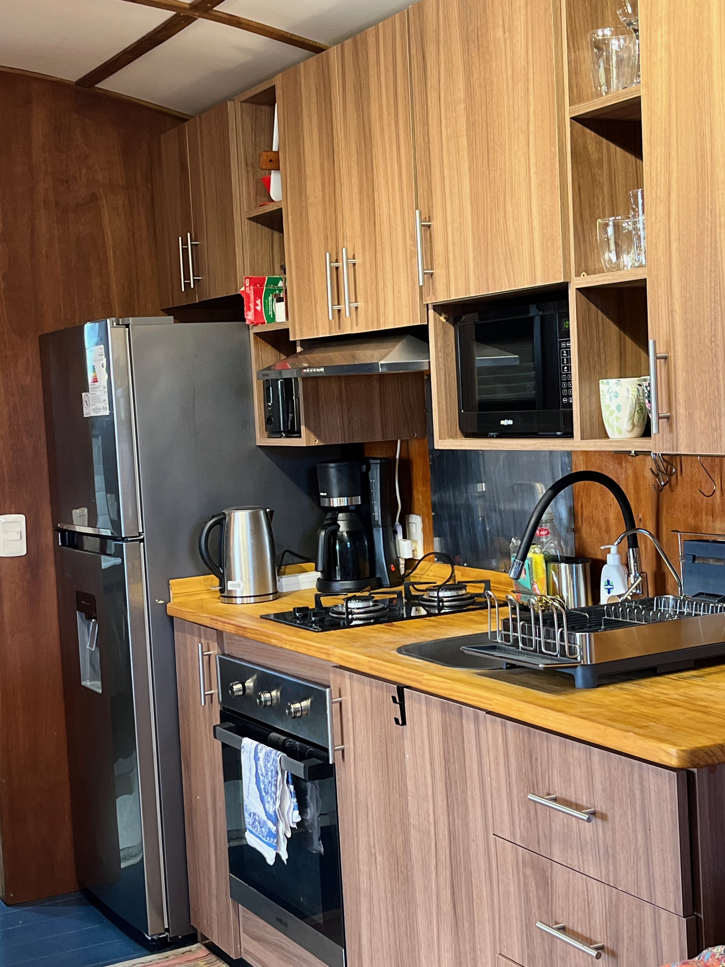 Kitchen with wooden cabinets, stainless steel refrigerator, microwave, coffee maker, electric stove, sink, and various kitchen items.