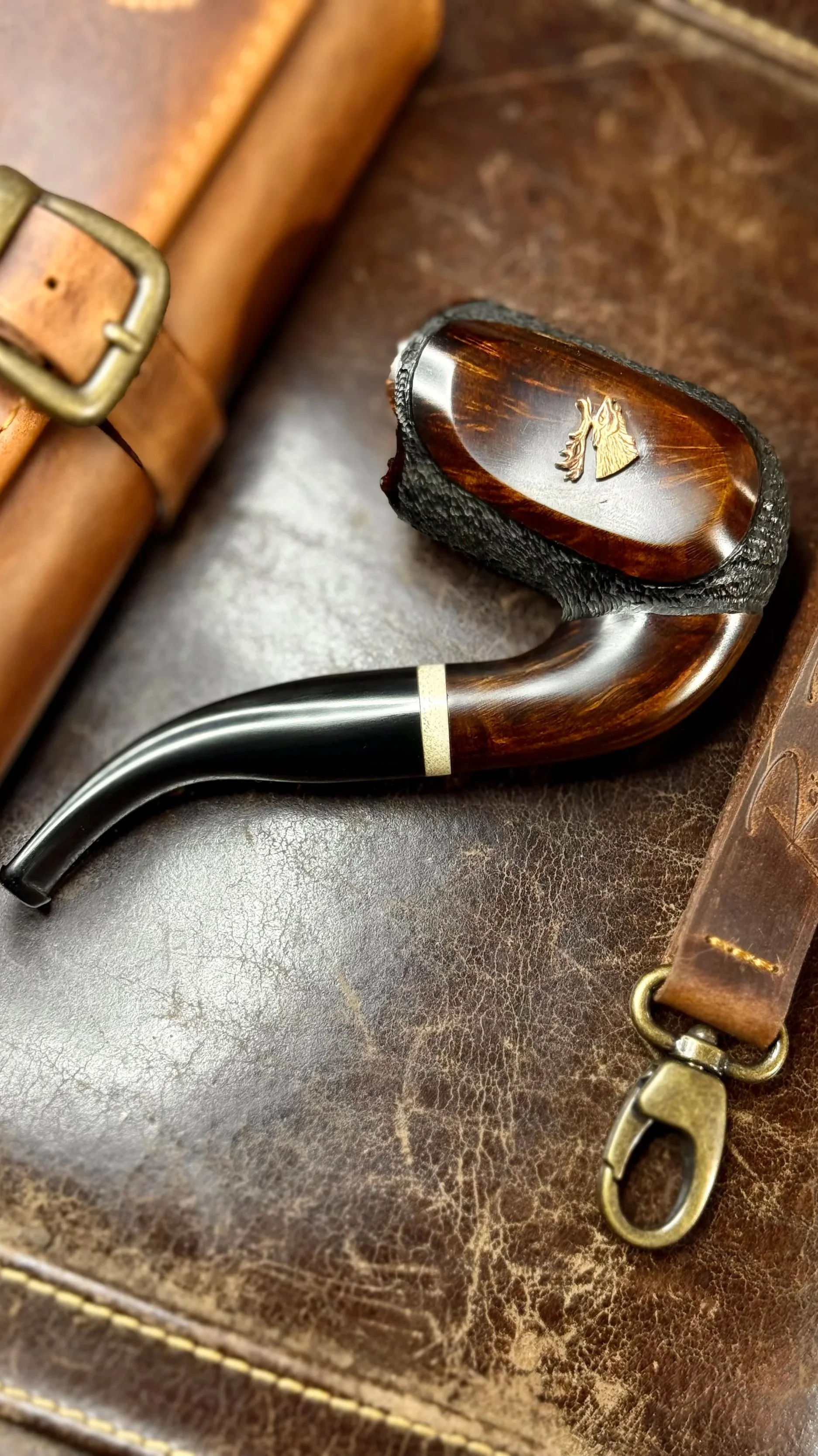 Luxury handmade briar tobacco pipe from the Riberg MP Wildlife Series, crafted in Estonia and inspired by forests, wildlife, and nature. a leather pipe with a deer head emblem, a leather belt, and a leather bag.