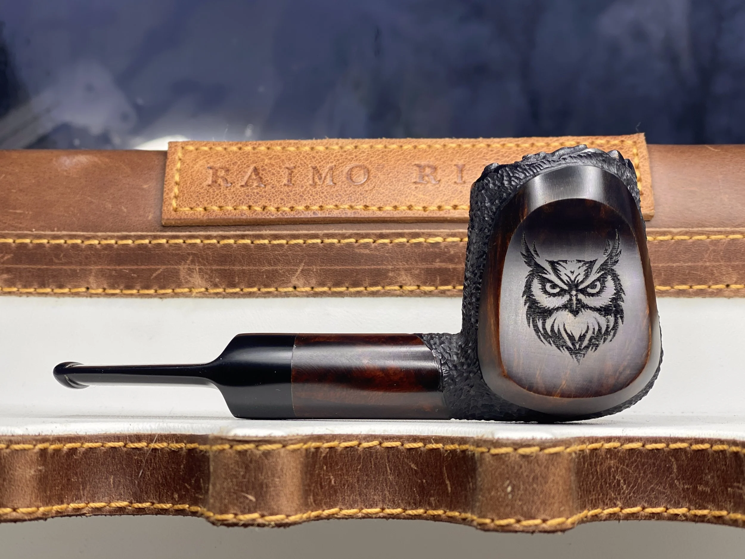 Handmade wooden smoking pipe with an owl engraving, displayed on a leather case.