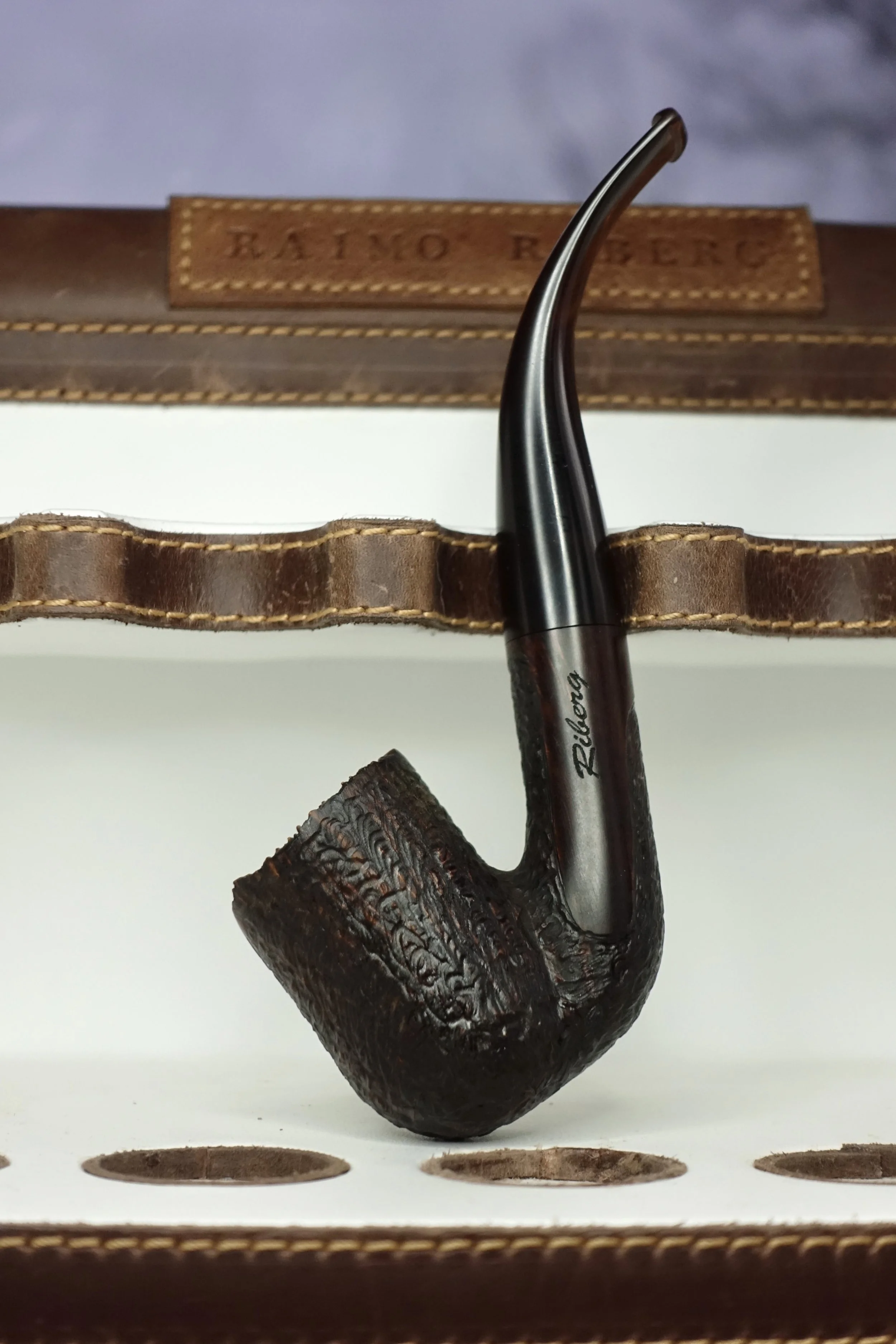 A rustic tobacco pipe with a curved stem and textured bowl, set against a leather backdrop.