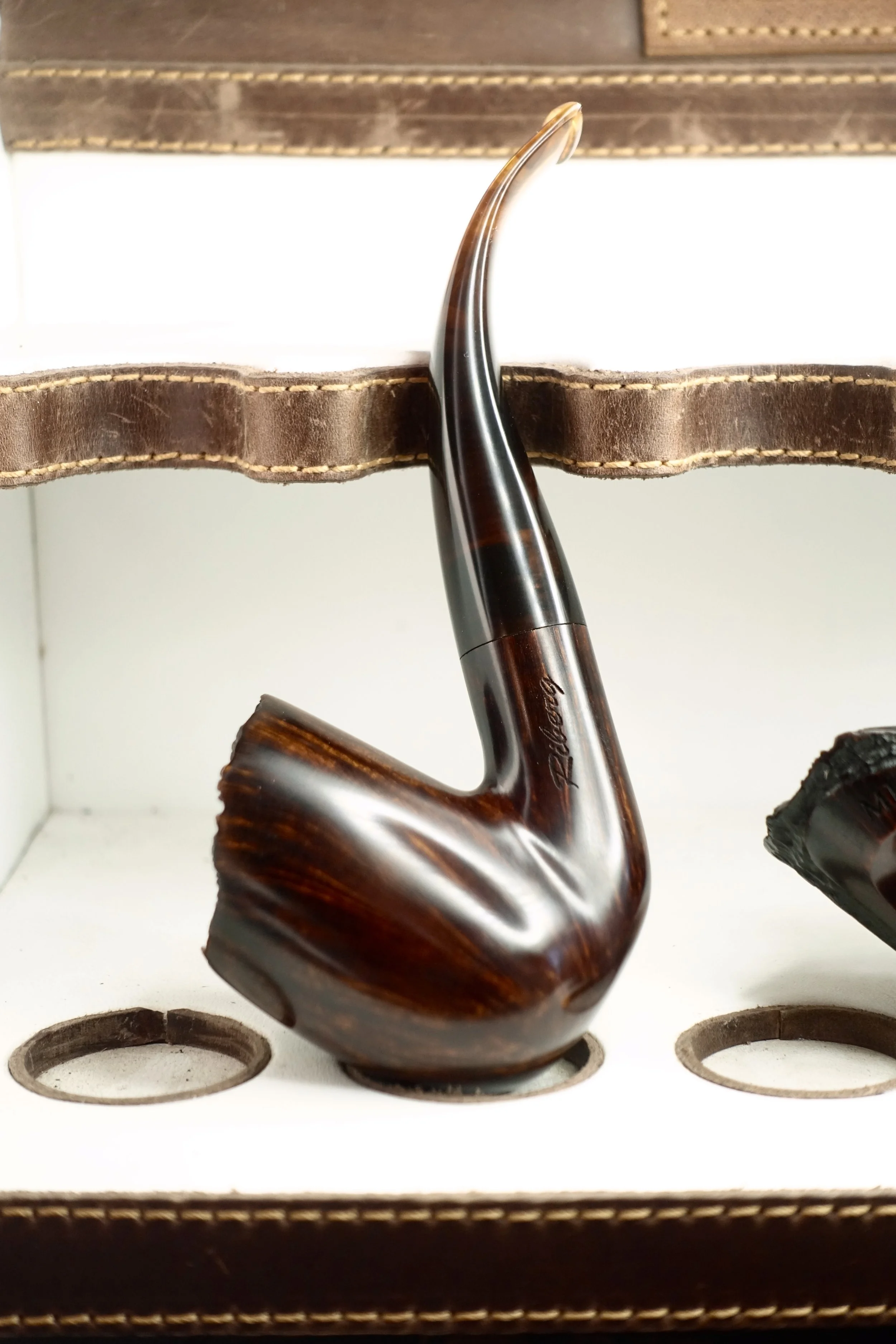 Unique, handcrafted wooden smoking pipe, glossy finish, displayed on leather and wood surface.