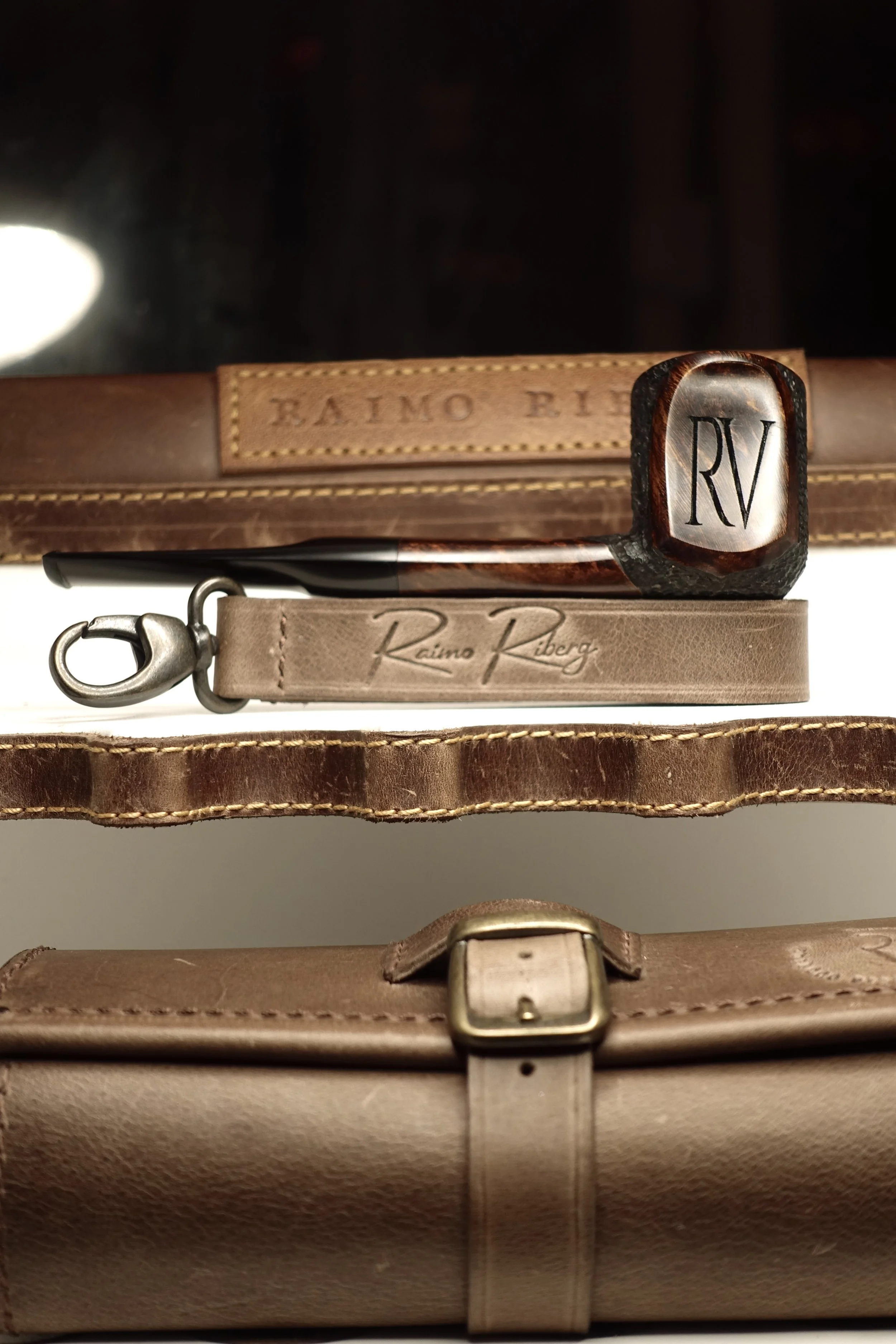 Luxury leather pipe case with a tobacco pipe and RV initials embossed, featuring a leather keychain and buckle detail.