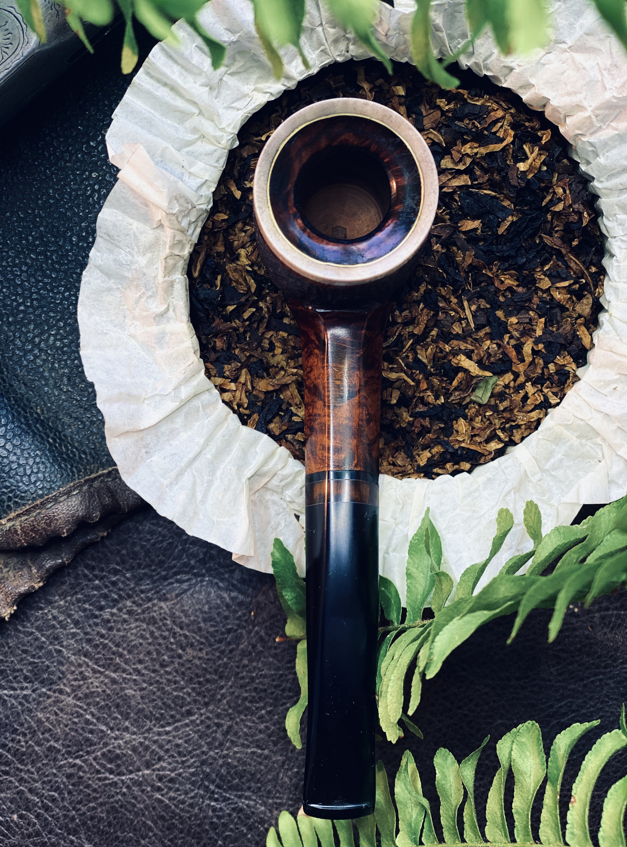 Wooden tobacco pipe next to dried tobacco leaves and green fern leaves