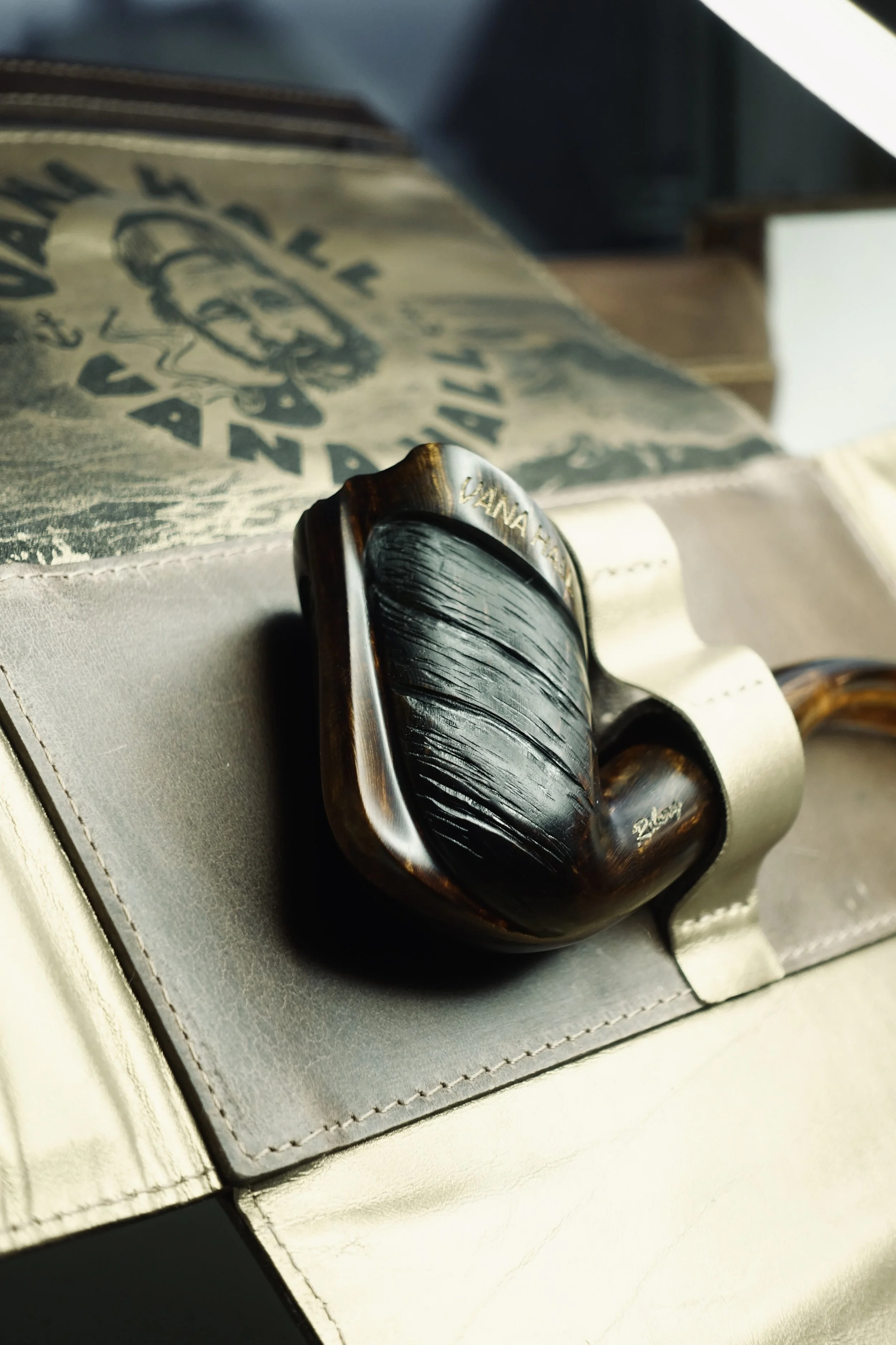 Close-up of a vintage smoking pipe with a dark, textured bowl and a light-colored stem, resting on a surface with a box underneath.