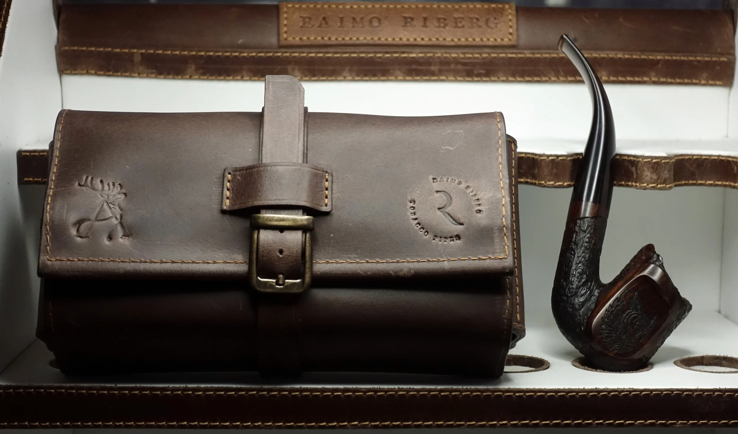 Brown leather tobacco pouch and smoking pipe displayed in a case.
