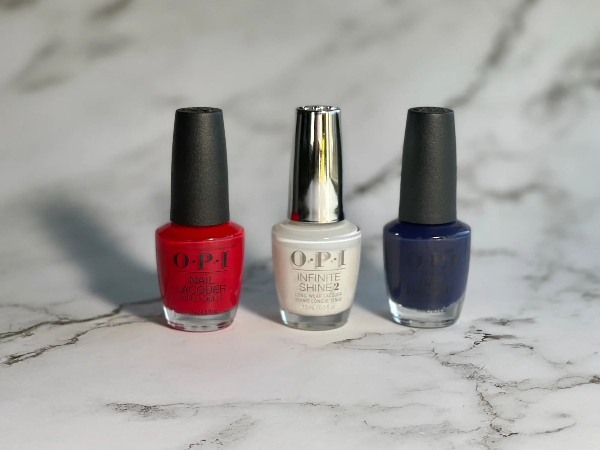 Photo of OPI Big Apple Red, Funny Bunny Infinite Shine, and Isn’t it Grand Avenue on grey marble background