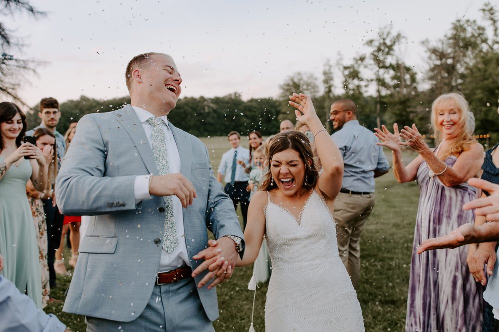 Couple laughs under guests throwing rice during exit